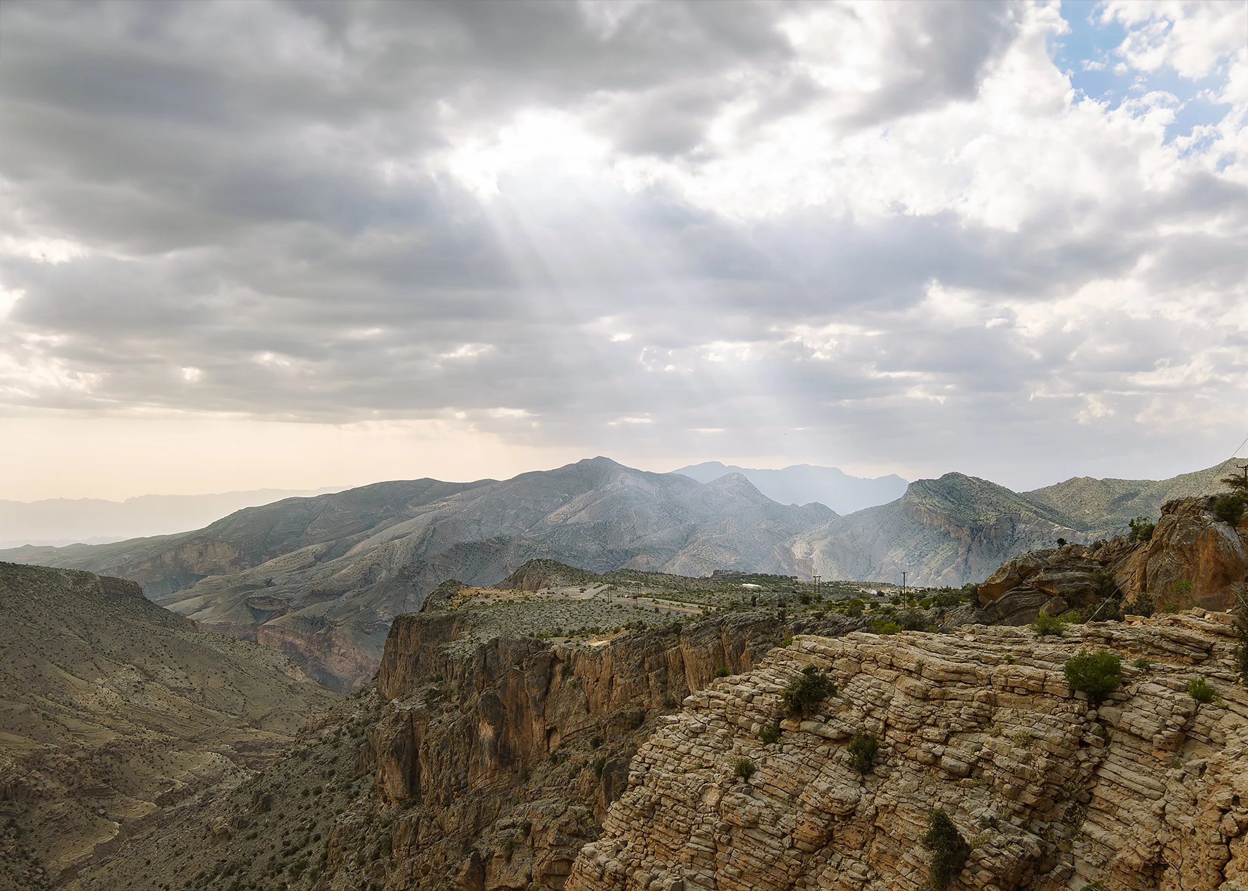 Mountain landscape with rocky cliffs and a cloudy sky with sun rays.