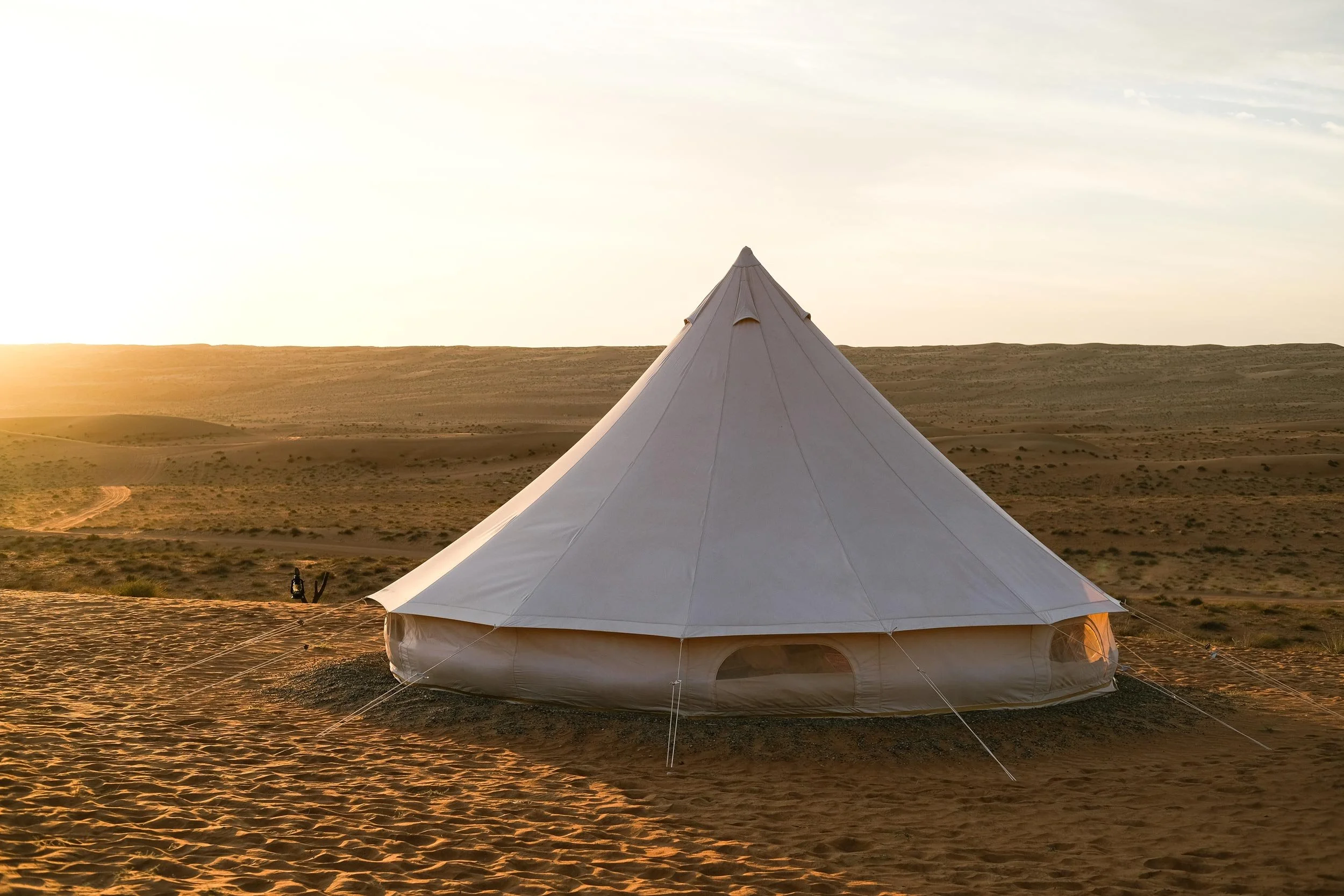 A white, cone-shaped tent set up in a desert landscape during sunset.