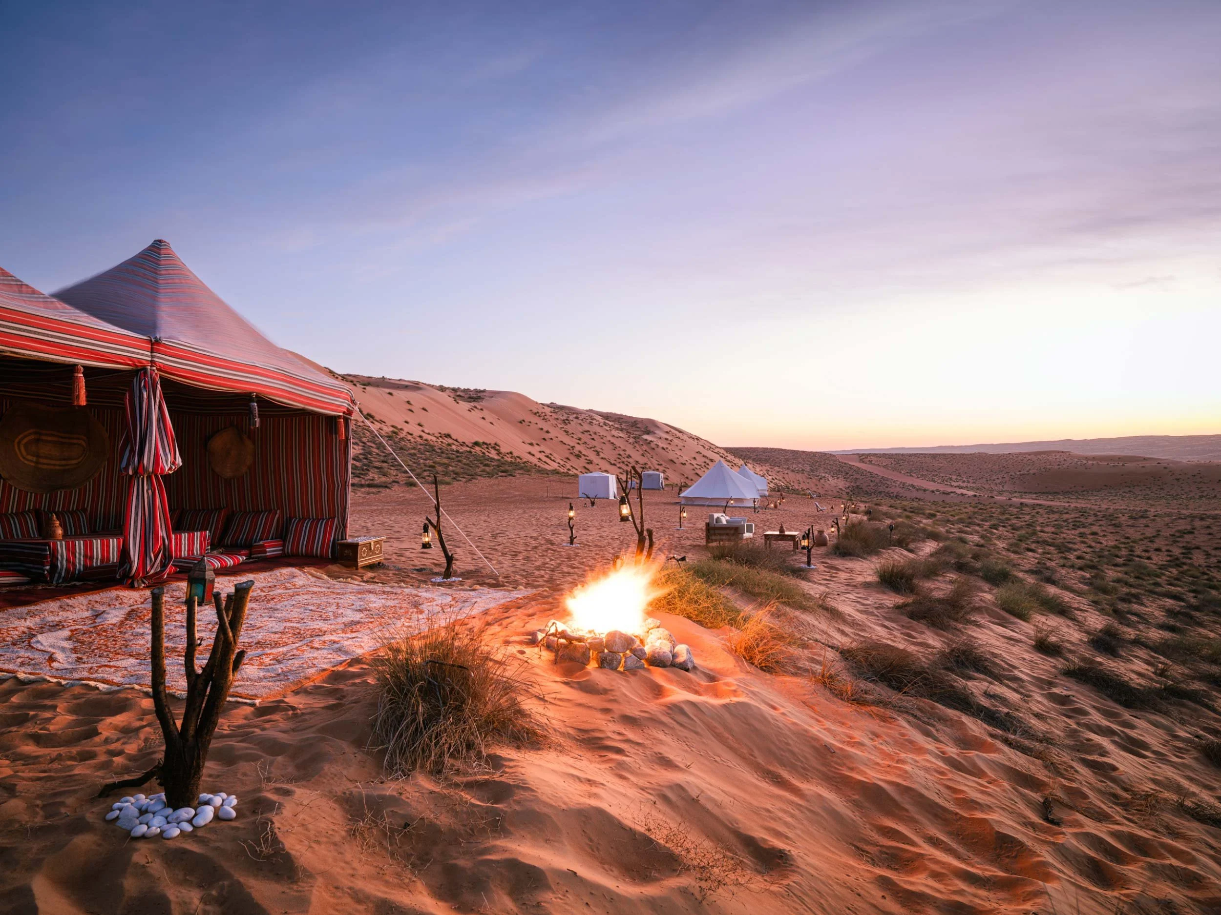 Desert scene at sunset with tents, a fire, and lounge furniture in the sand dunes in Wahiba Sands - Biddiyah - Oman.