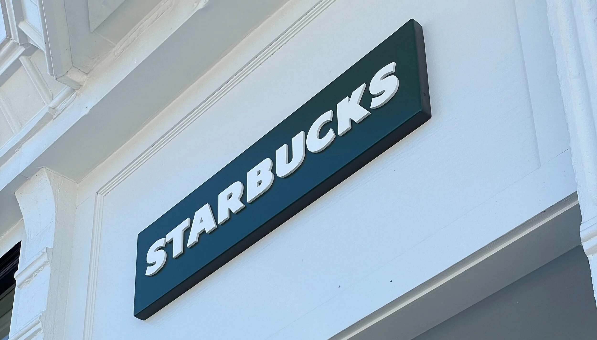 Street sign reading 'Starbucks' mounted on a white building exterior.