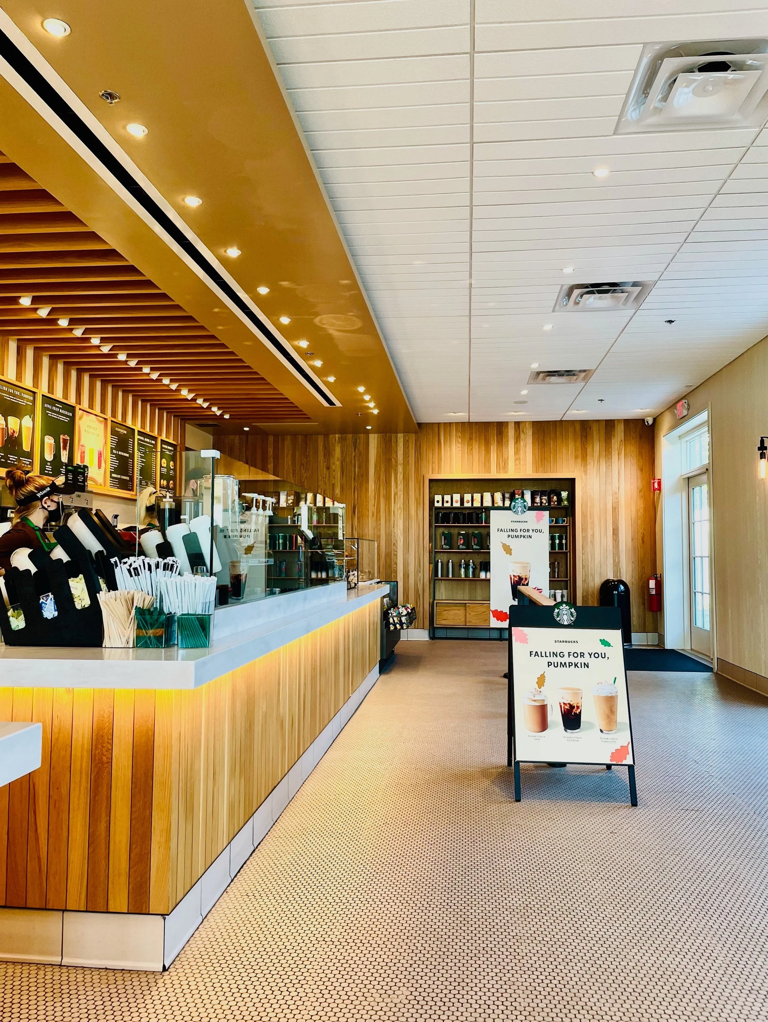 Interior of a Starbucks coffee shop with a wooden counter, menu boards, and promotional signs for fall drinks on a stand.
