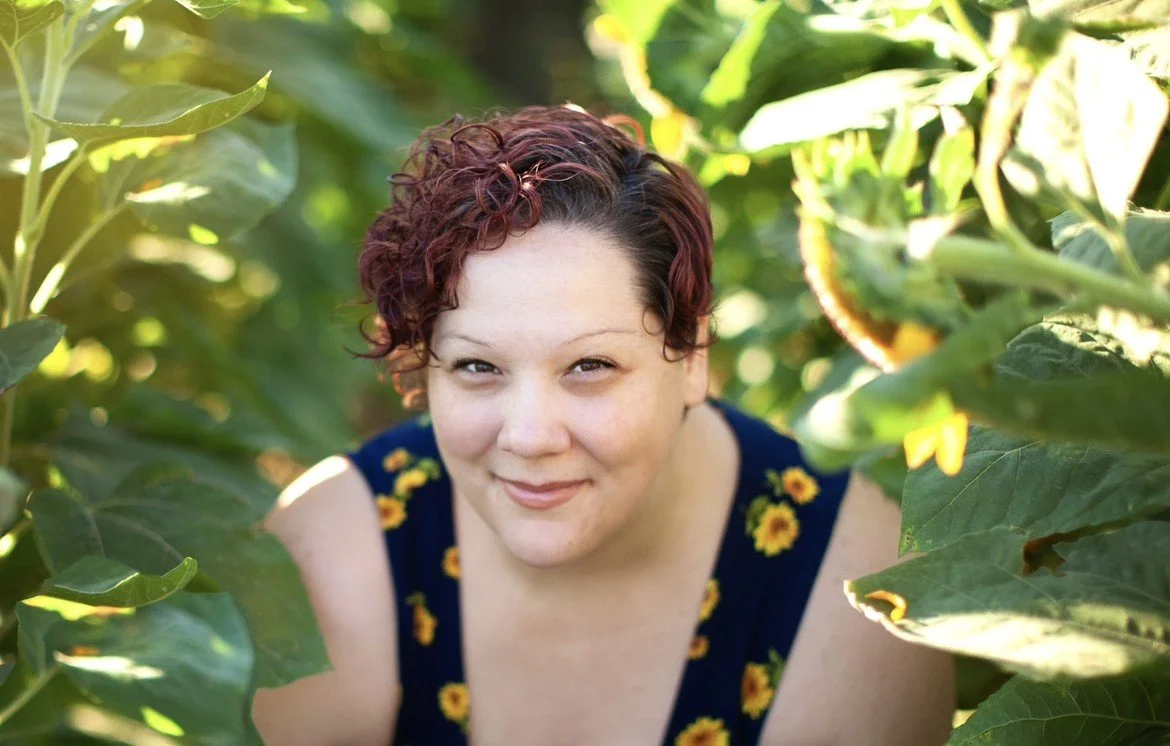 Kandace Ledergerber, LPC and Certified EMDR Therapist offering EMDR therapy in Phoenix, AZ, smiling in a sunlit field of greenery wearing a navy blue tank top with sunflowers.