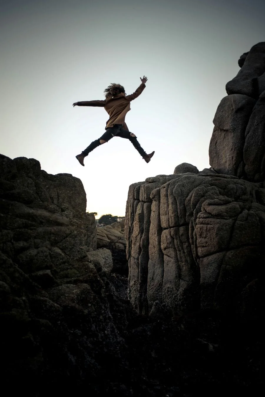 Person jumping across rocks at sunset, representing facing fear and taking steps toward healing with therapy