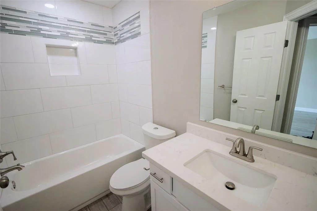 White bathtub and shower surround with accent tiling.
