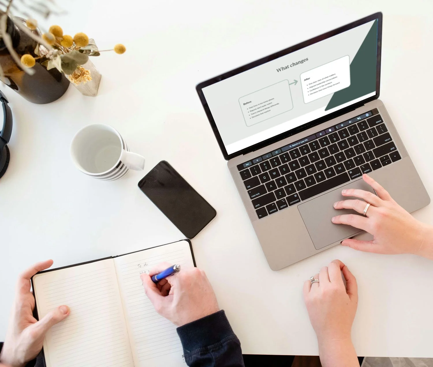 Two people hands in view, one using using a laptop, the other a notebook.