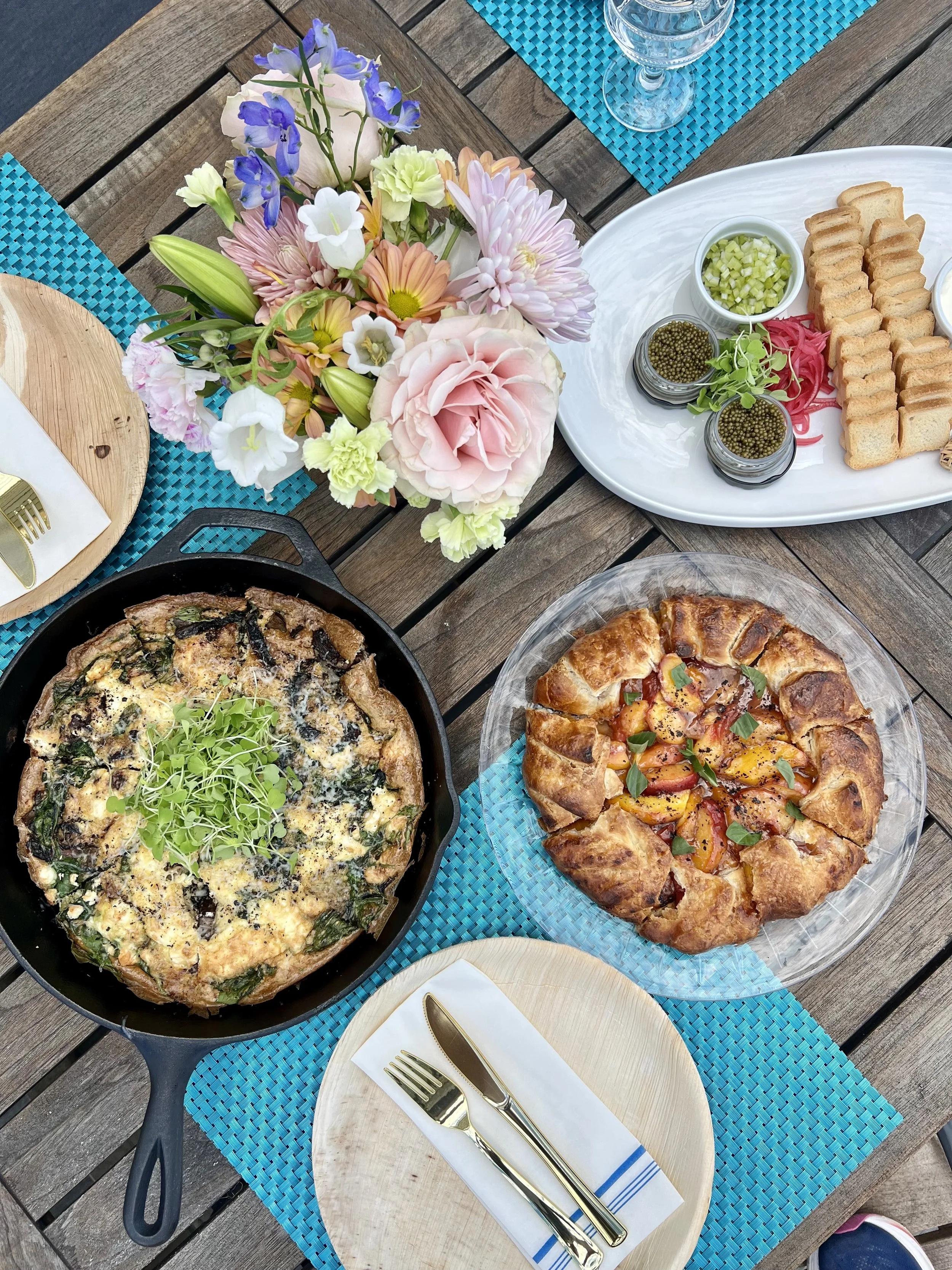 Table with a pan of frittata on the table, peach pastry, caviar board, and flowers.