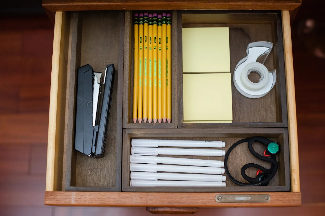 Well-organized office drawer with dividers containing pencils, pens, Post-its, tape, a stapler, and other office essentials. 