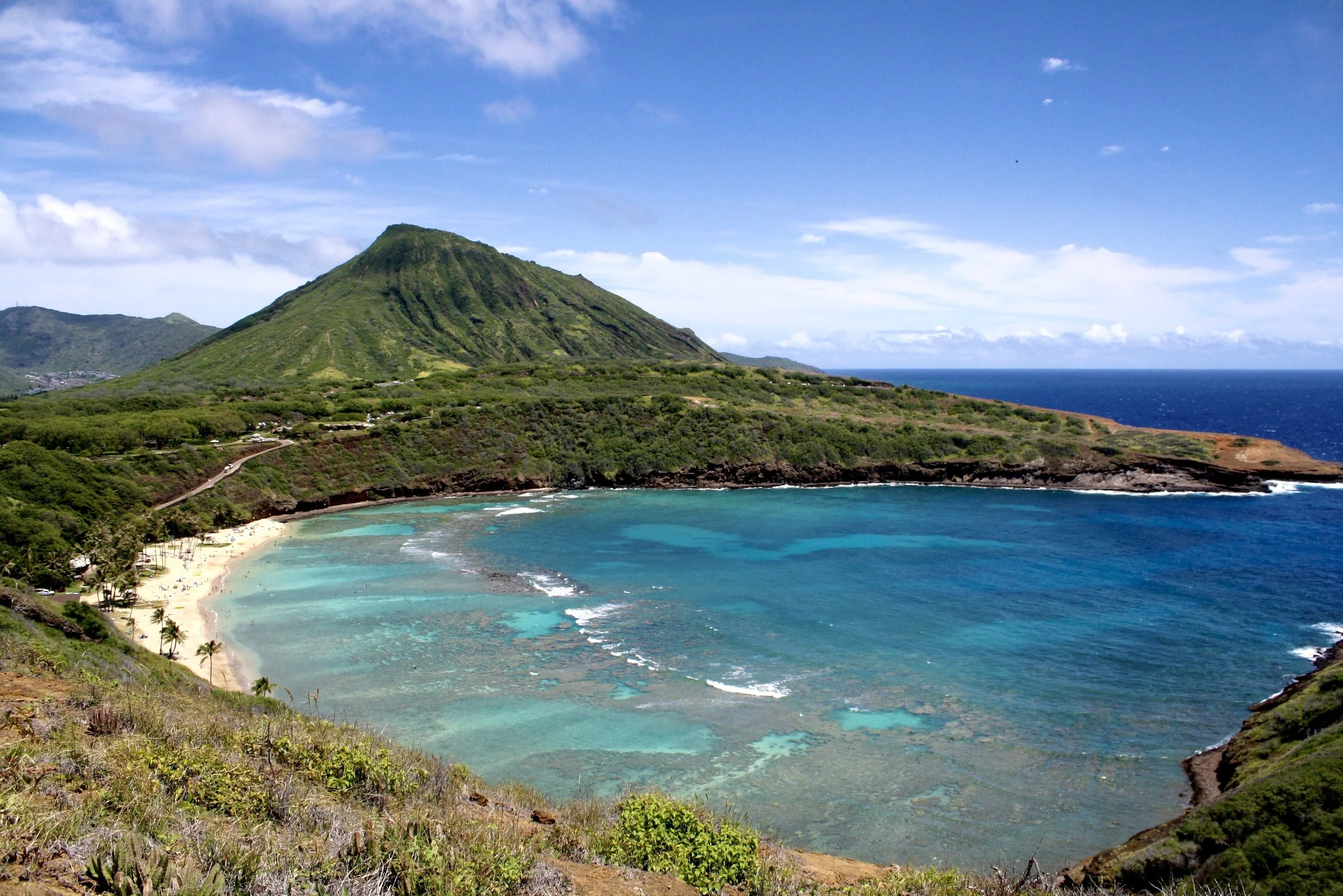 Aerial view of Hanauma Bay, a turquoise beach surrounded by a lush green mountain and rocky cliffs.