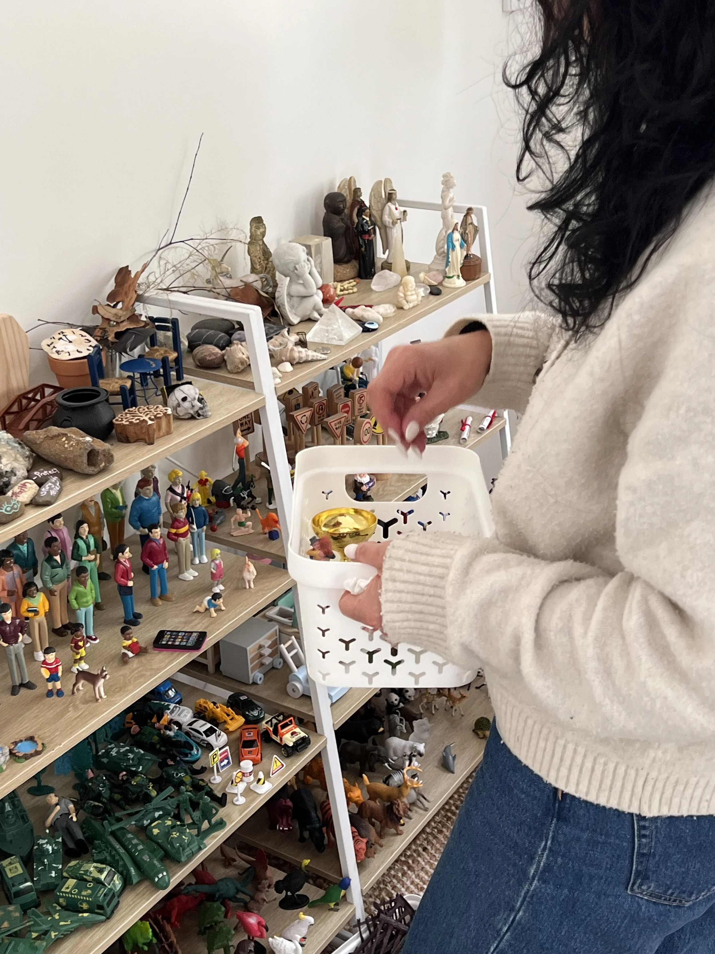 Person shopping for small figurines and toys at a display in a store, with shelves filled with various figurines, stones, and collectibles.