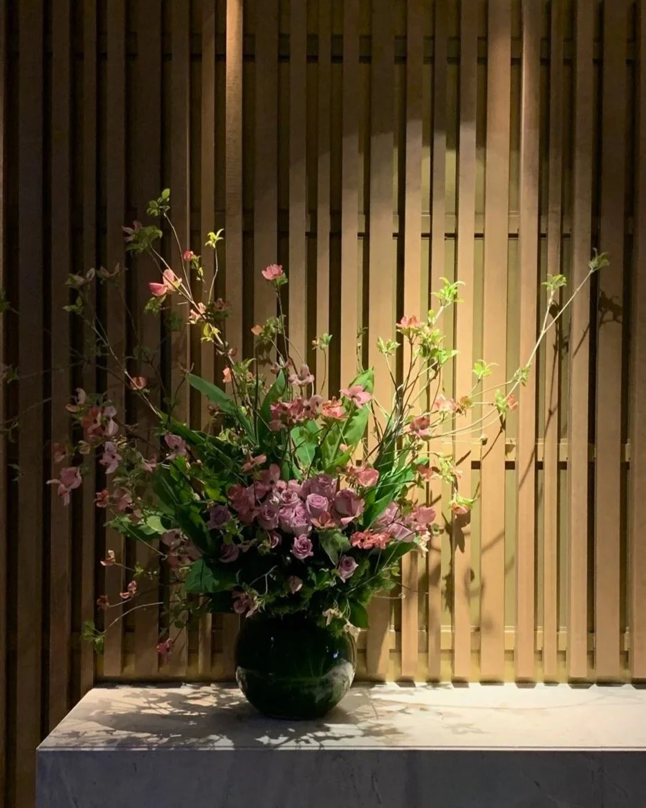 Large fishbowl vessel filled with green arum lillies, mauve roses and blossom. Botanic Flowers 1300 820 920.