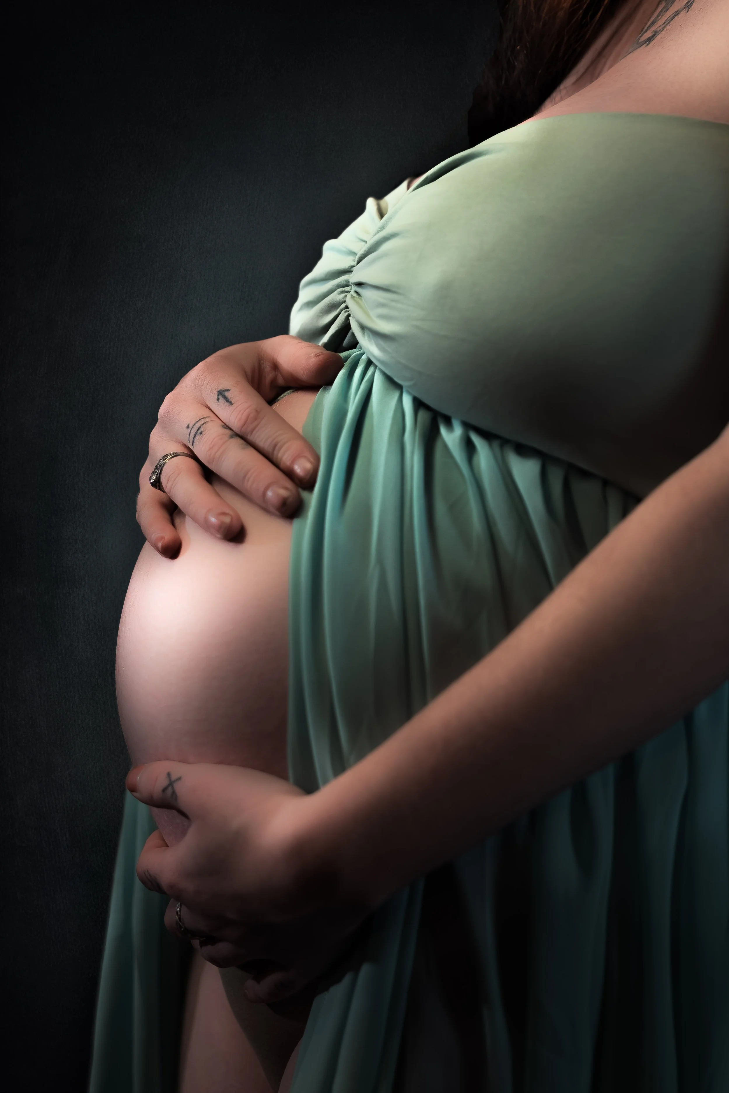 Expecting mother in a flowing green gown cradling her bump during a maternity boudoir session in Maine