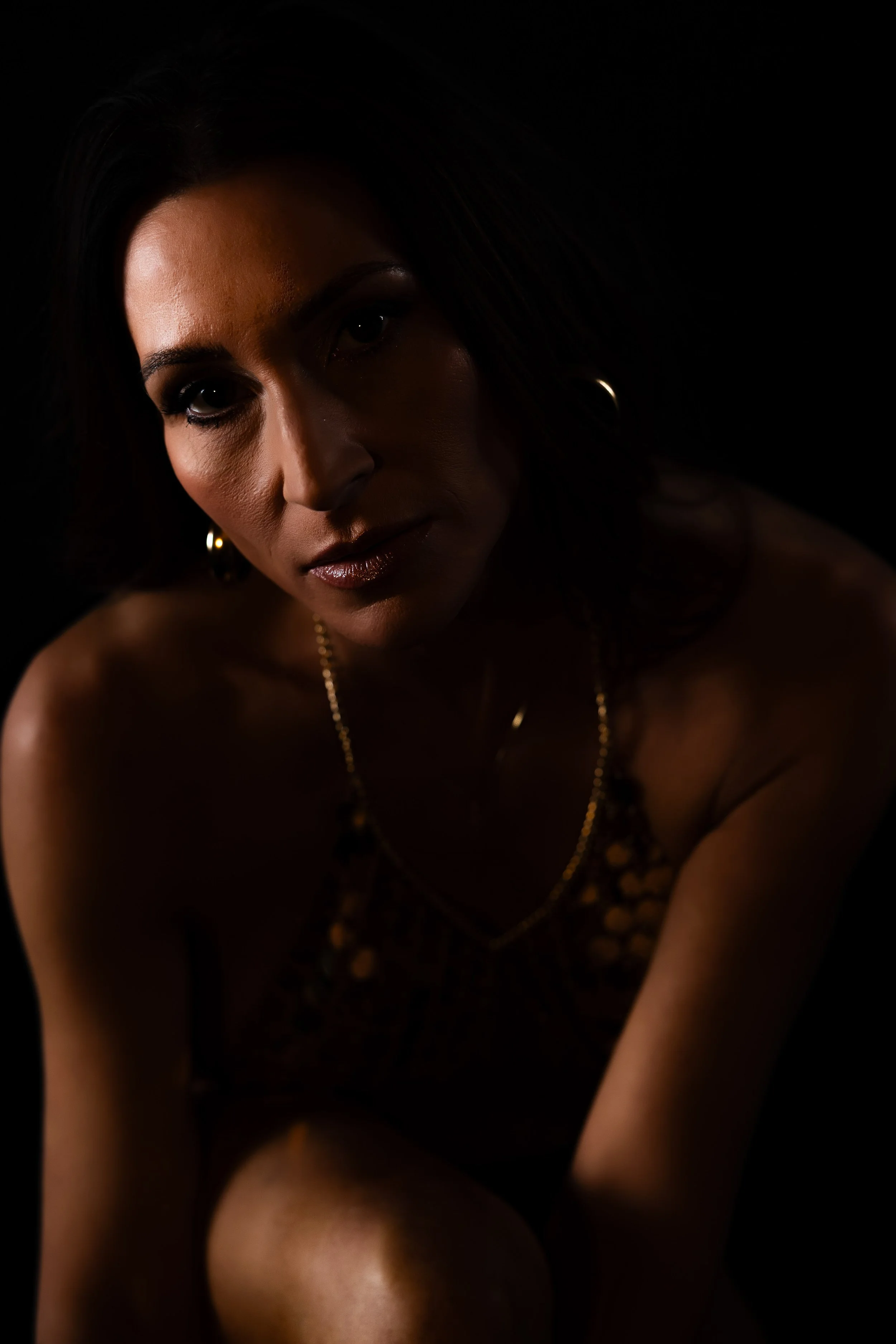 Woman with dark hair in warm, low light during a boudoir session in Maine