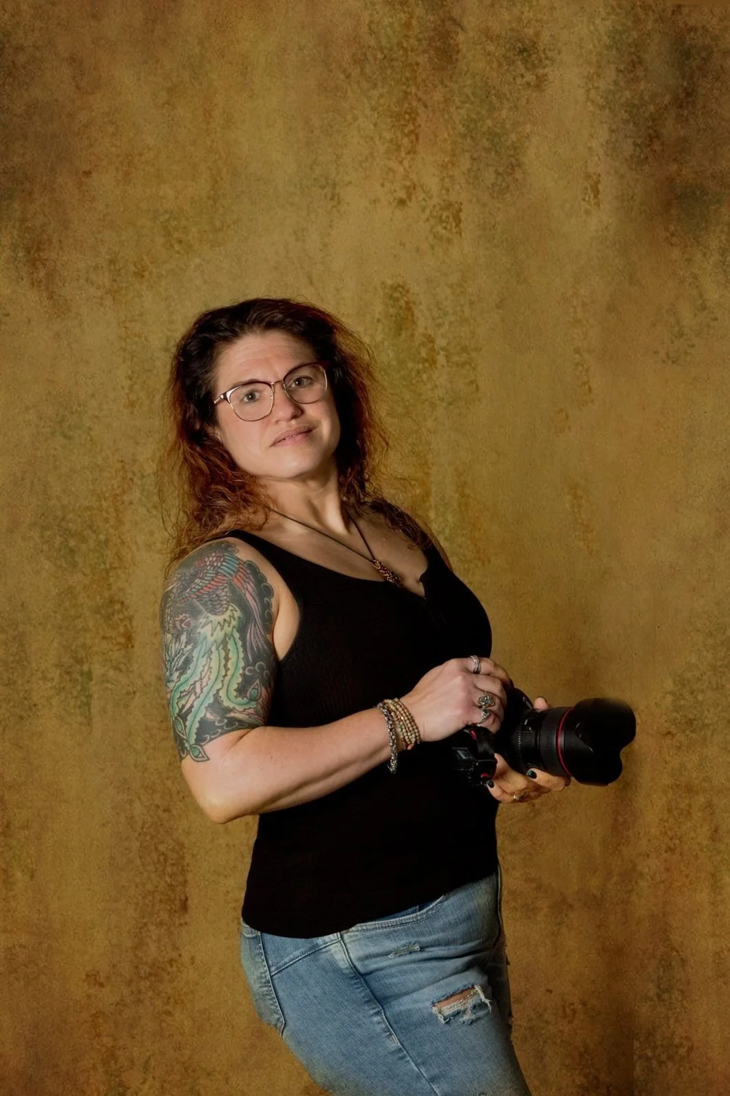 Jen Jackson, boudoir photographer at T3 Portraits, holding her camera in front of a gold backdrop
