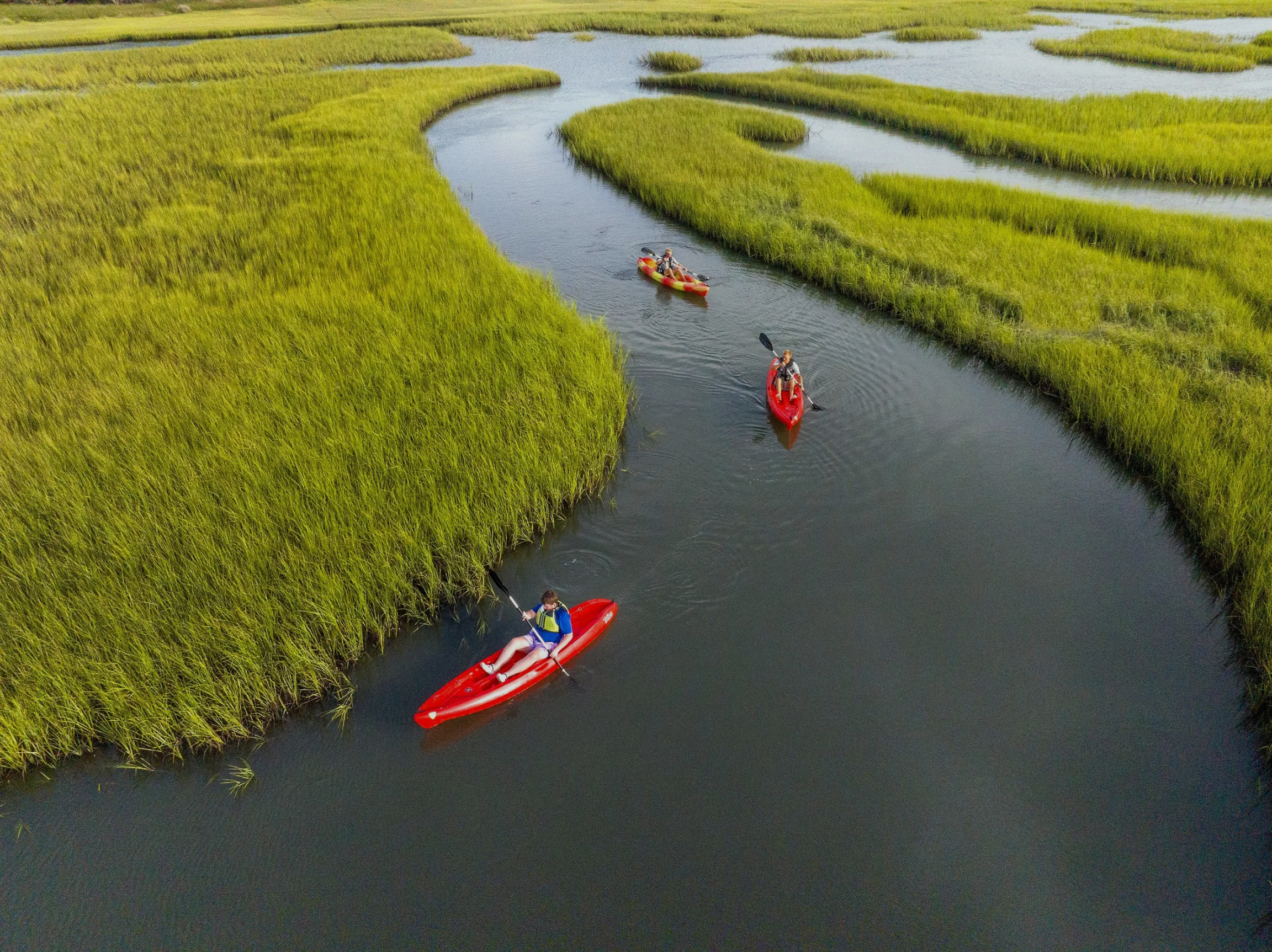 Family kayaking on a calm water body under cloudy sky, with two kayaks in the foreground and a person kayaking in the background.