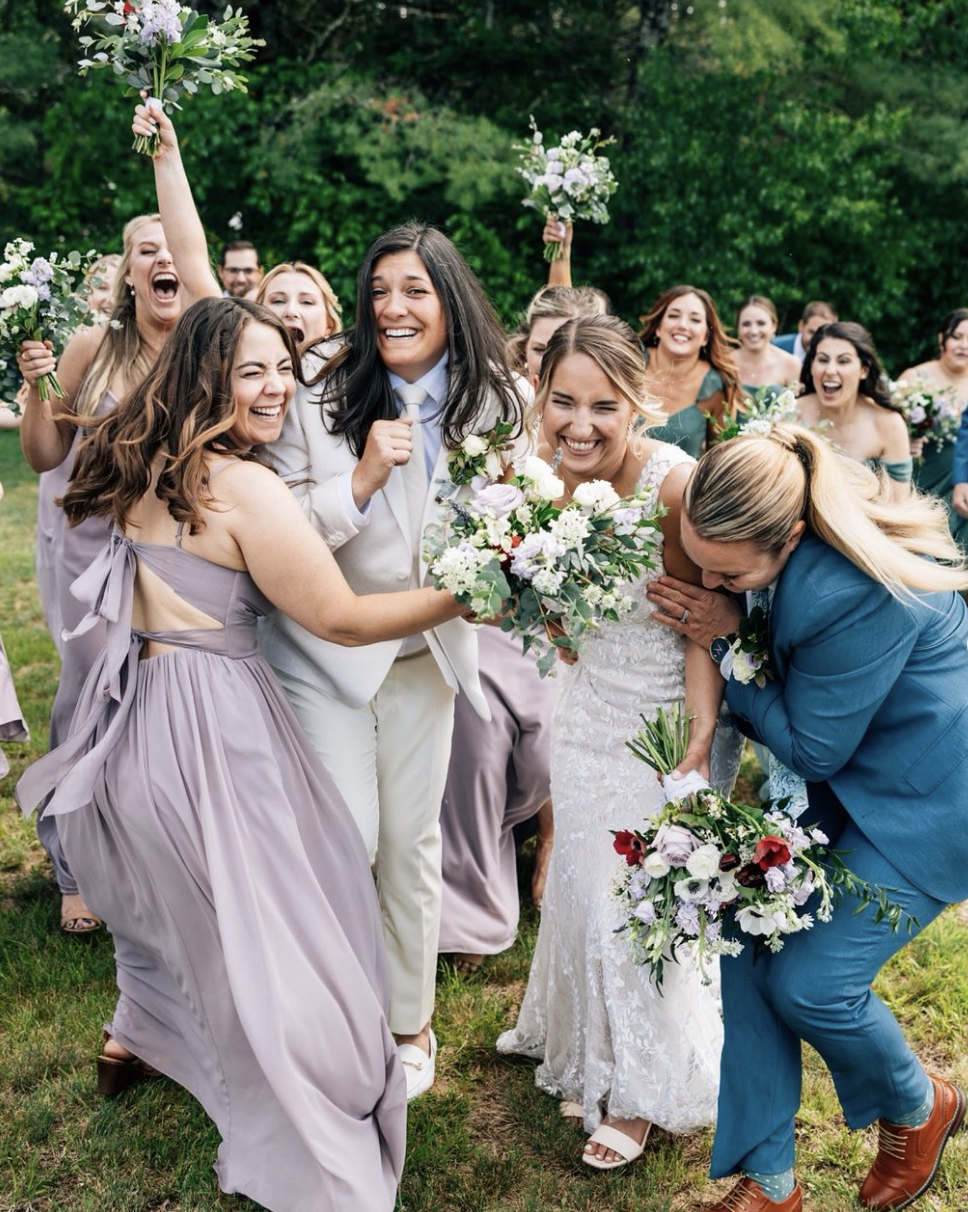 Joyful wedding celebration outdoors with bridesmaids and bride holding bouquets, laughing, and sharing a moment of happiness.