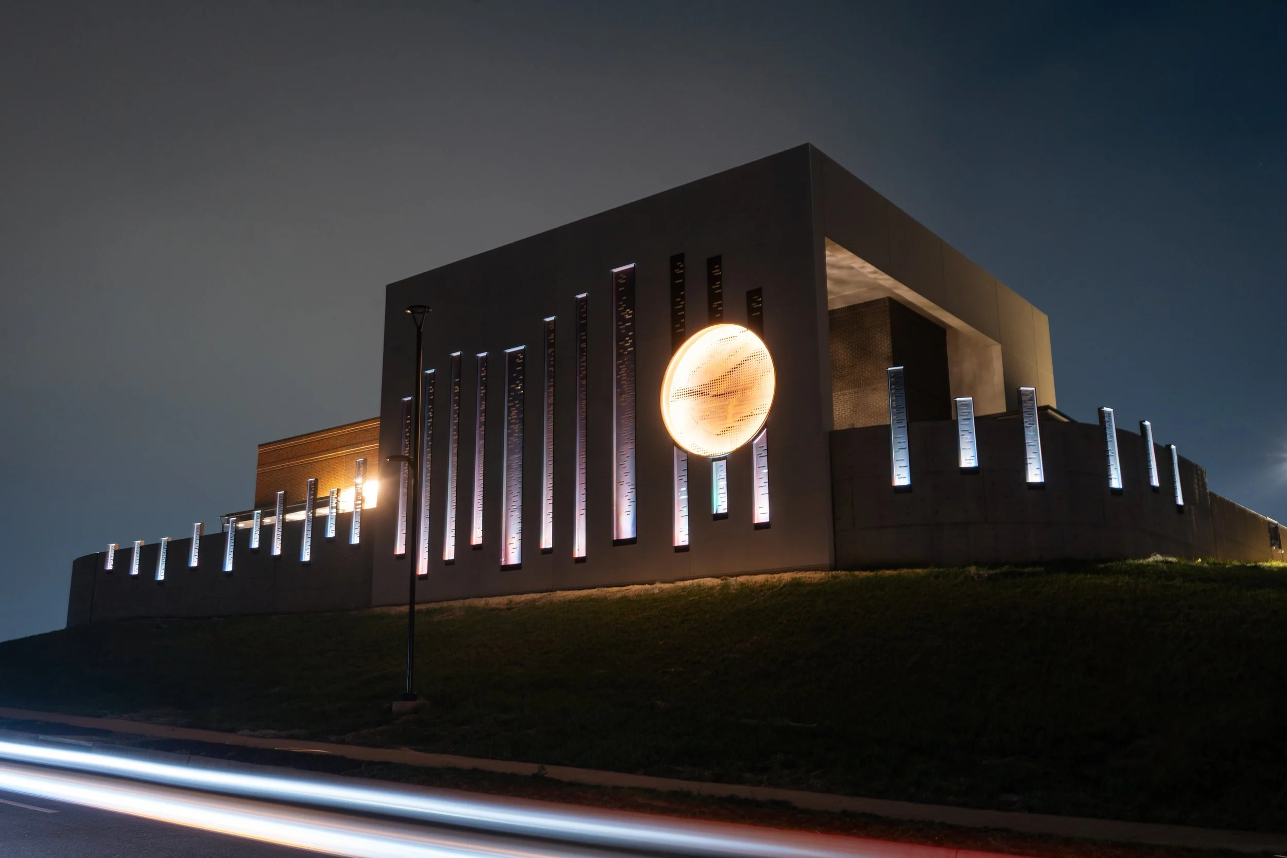 Modern building at night with illuminated geometric design, includes a large circular feature and tall vertical light strips.