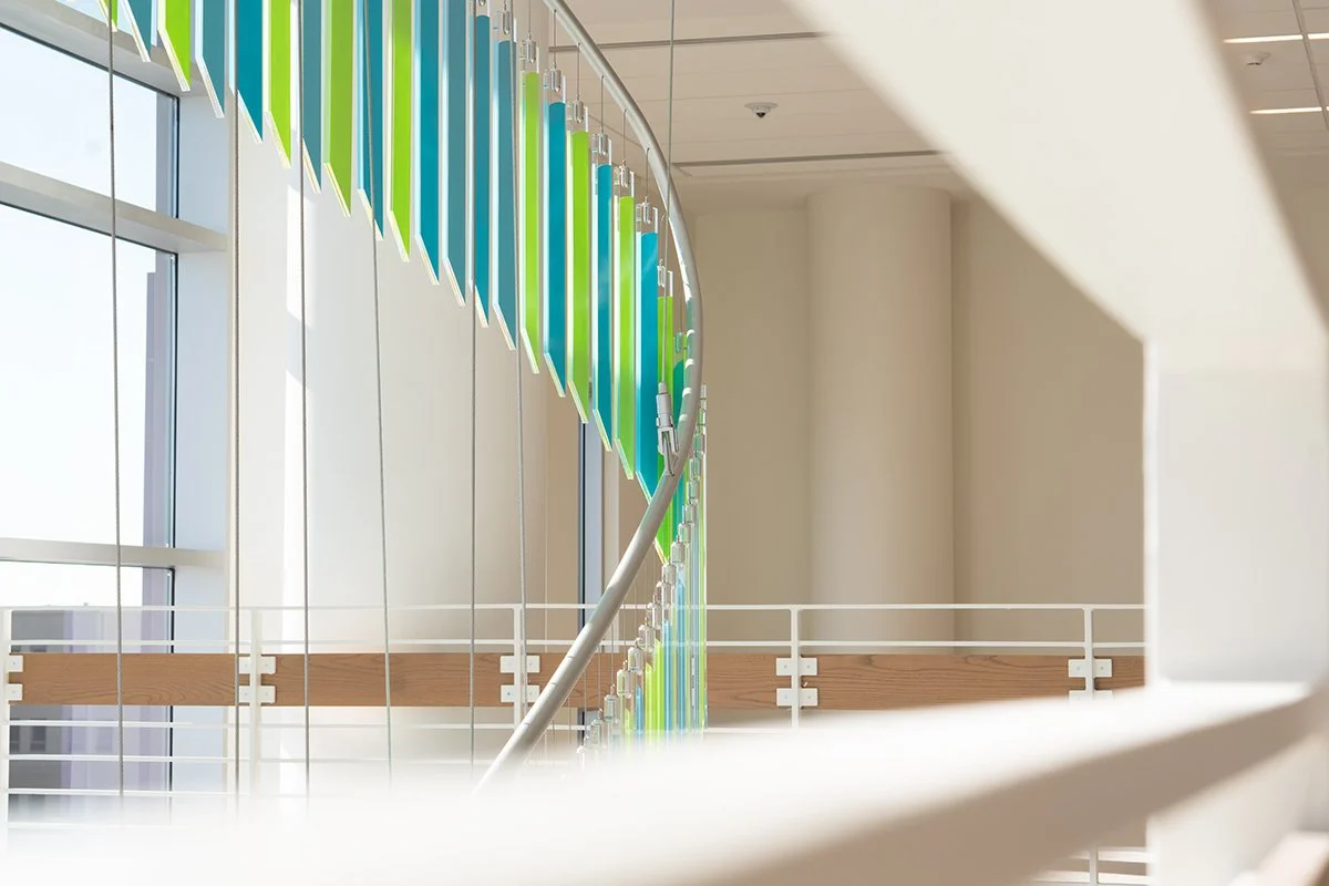 Modern indoor staircase with colorful glass panels in shades of blue and green, alongside a white metal railing.