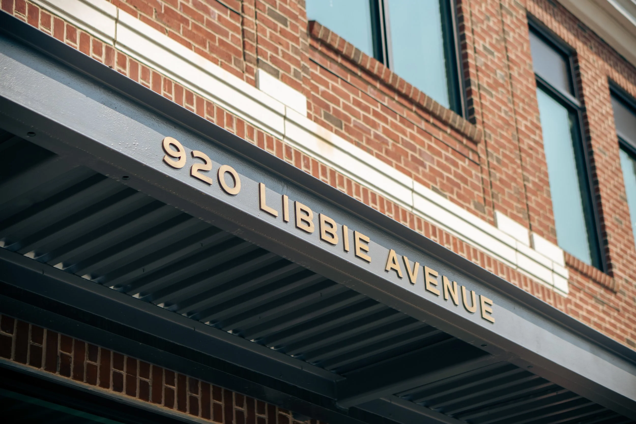 Street sign that reads '920 Lippie Avenue' mounted on a metal awning in front of a brick building with windows.