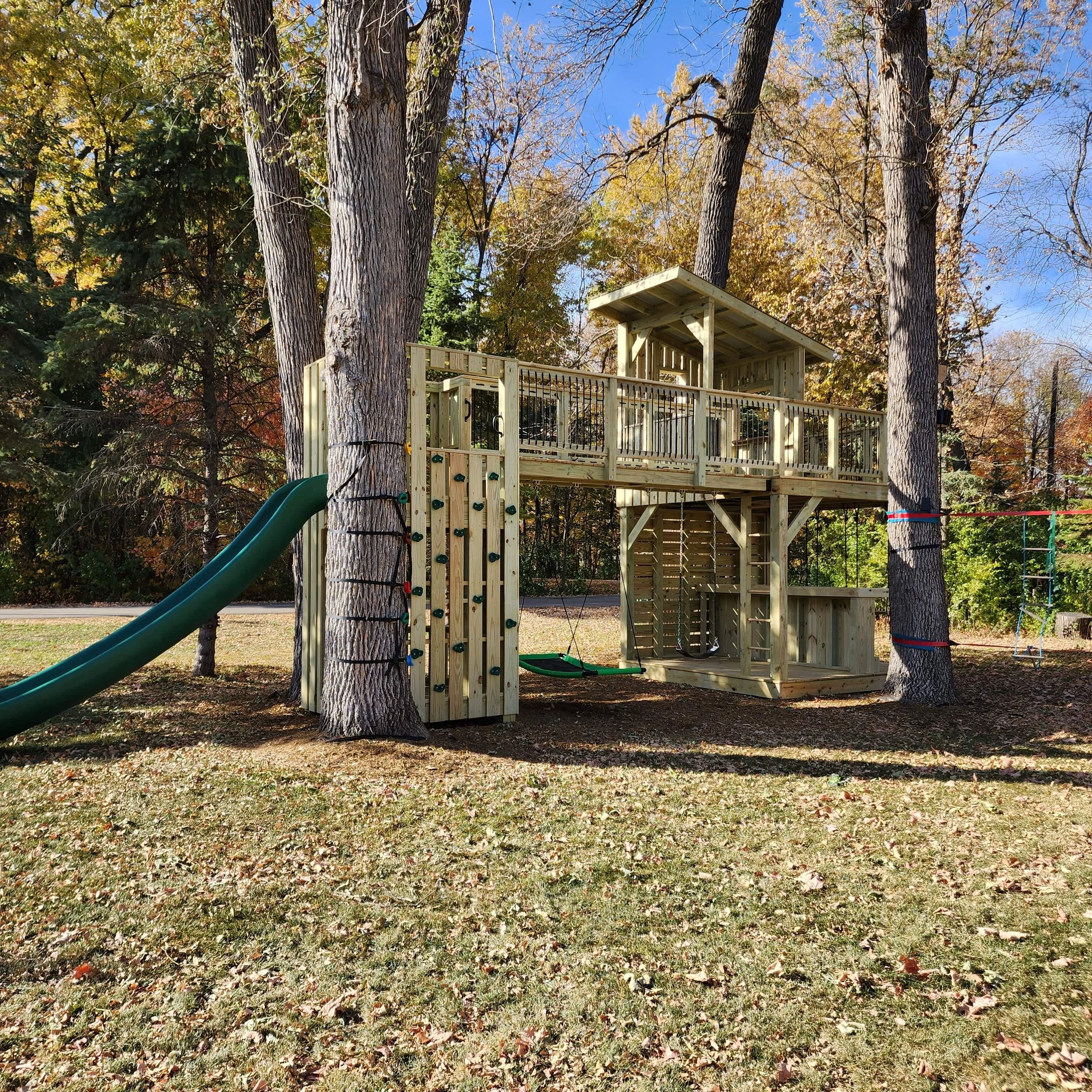 custom tree fort with green slide climbing wall clubhouse and bar