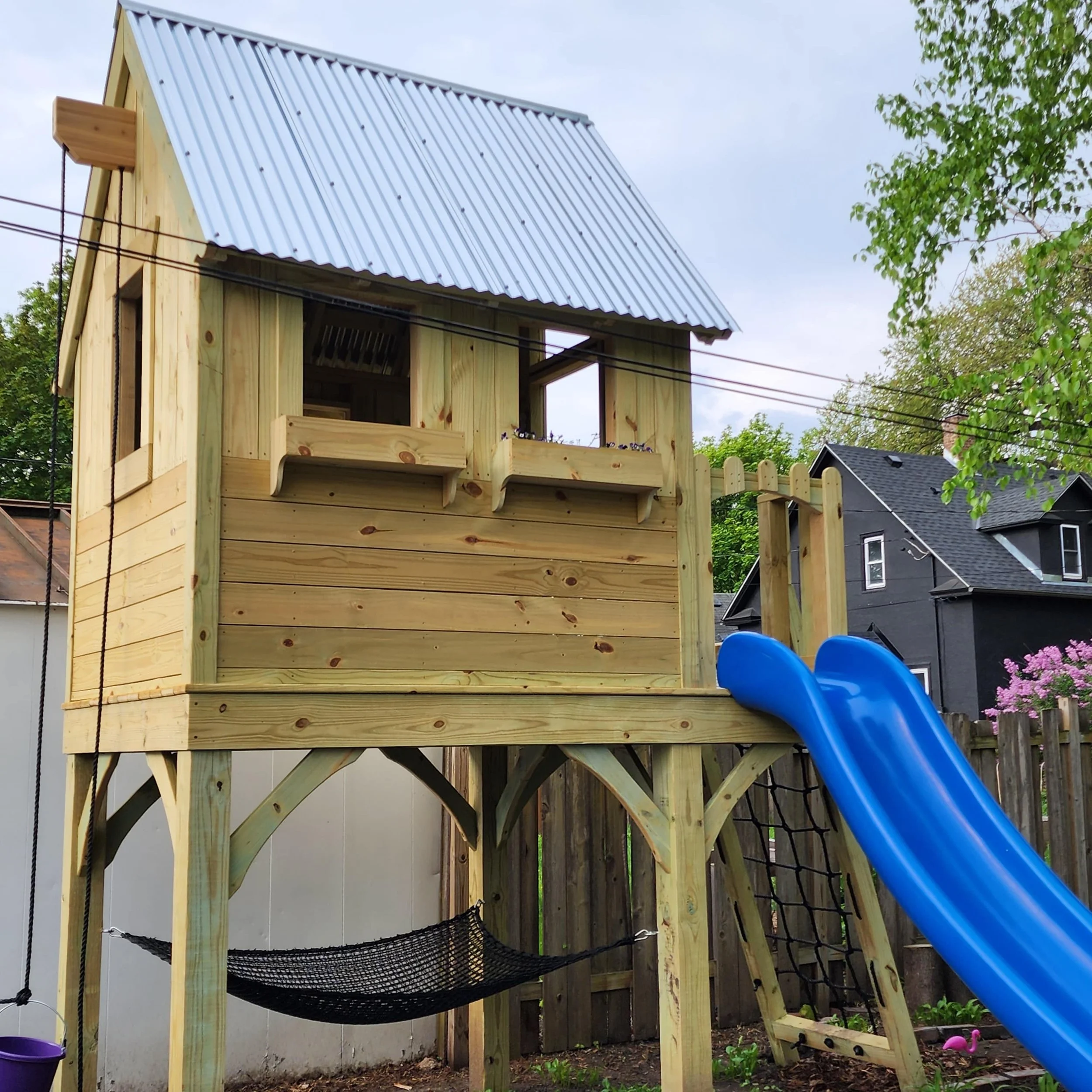 custom wood play structure with hammock underneath and blue slide