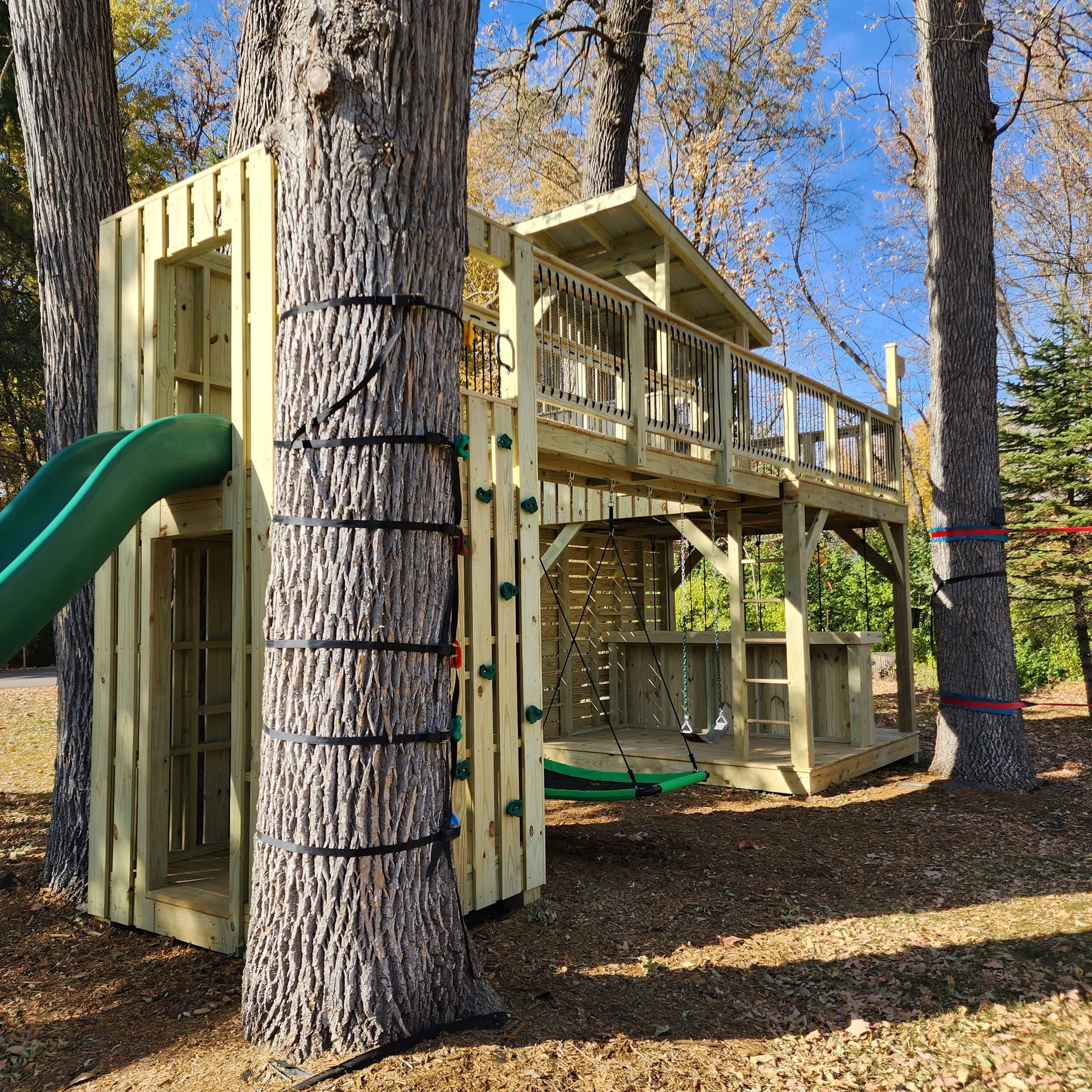 custom tree fort with green slide and bridge