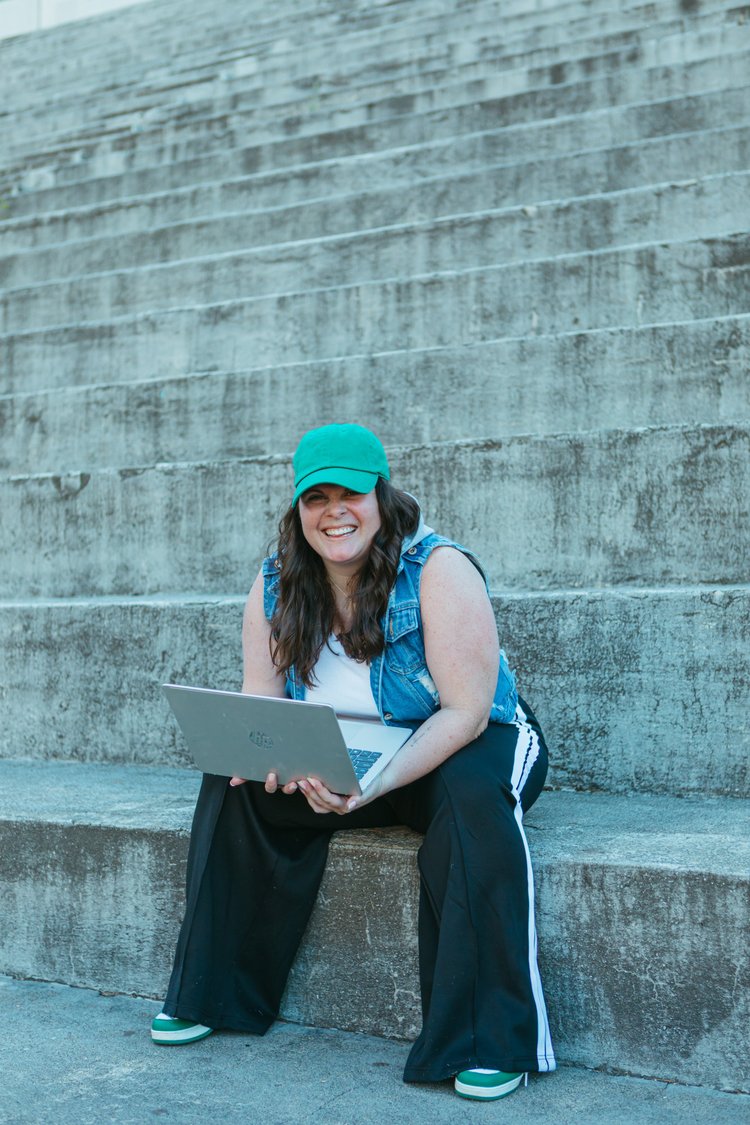 Ellyn sitting on the bleachers with her laptop, smiling