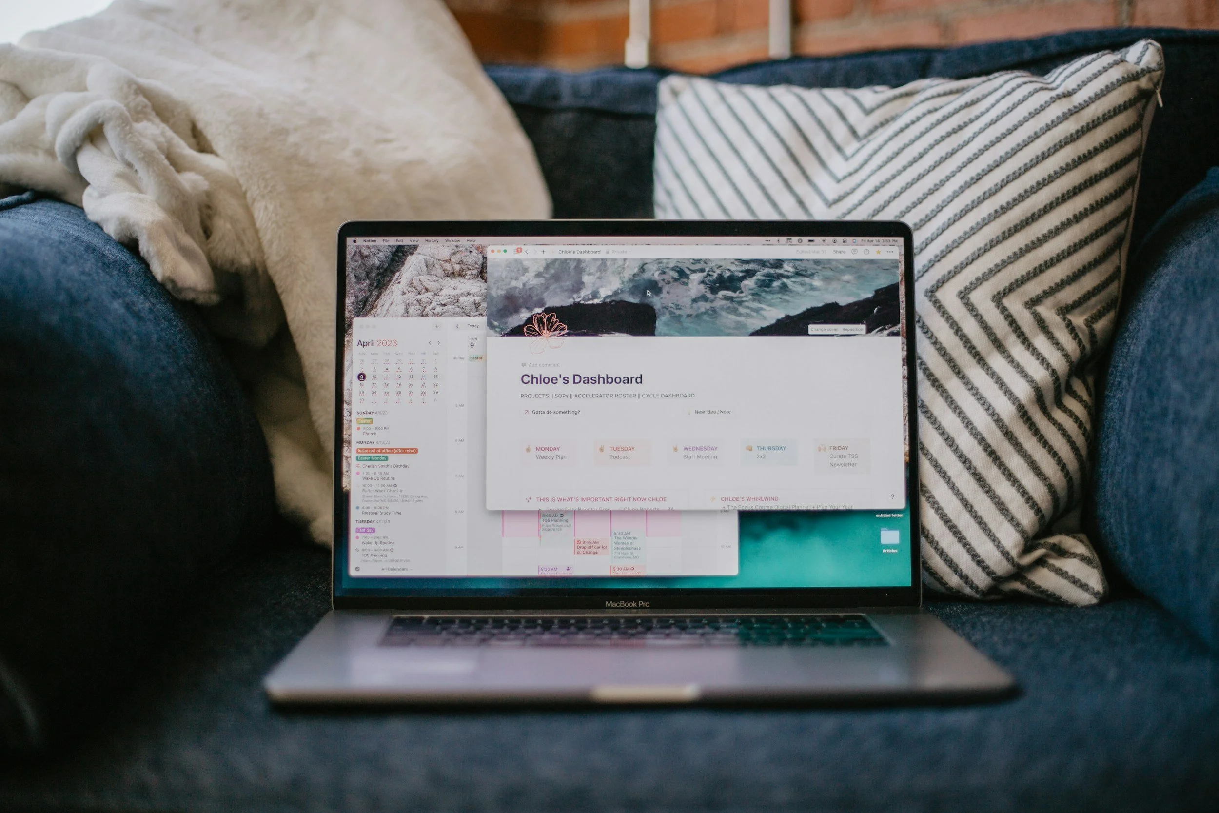 Open MacBook Pro on a couch displaying a digital calendar and a project dashboard with a background of ocean waves.