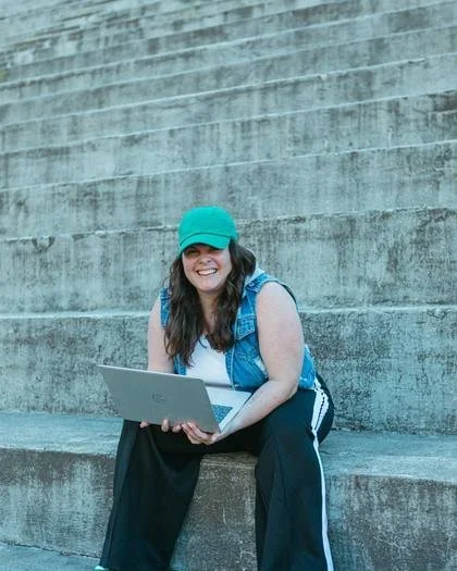Ellyn on the stadium steps with her laptop, smiling at the camera