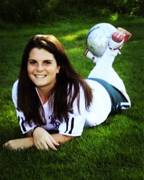 Younger Ellyn lying in the grass with a soccer ball