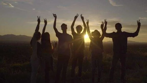 Teenagers facing sunset holding peace sign