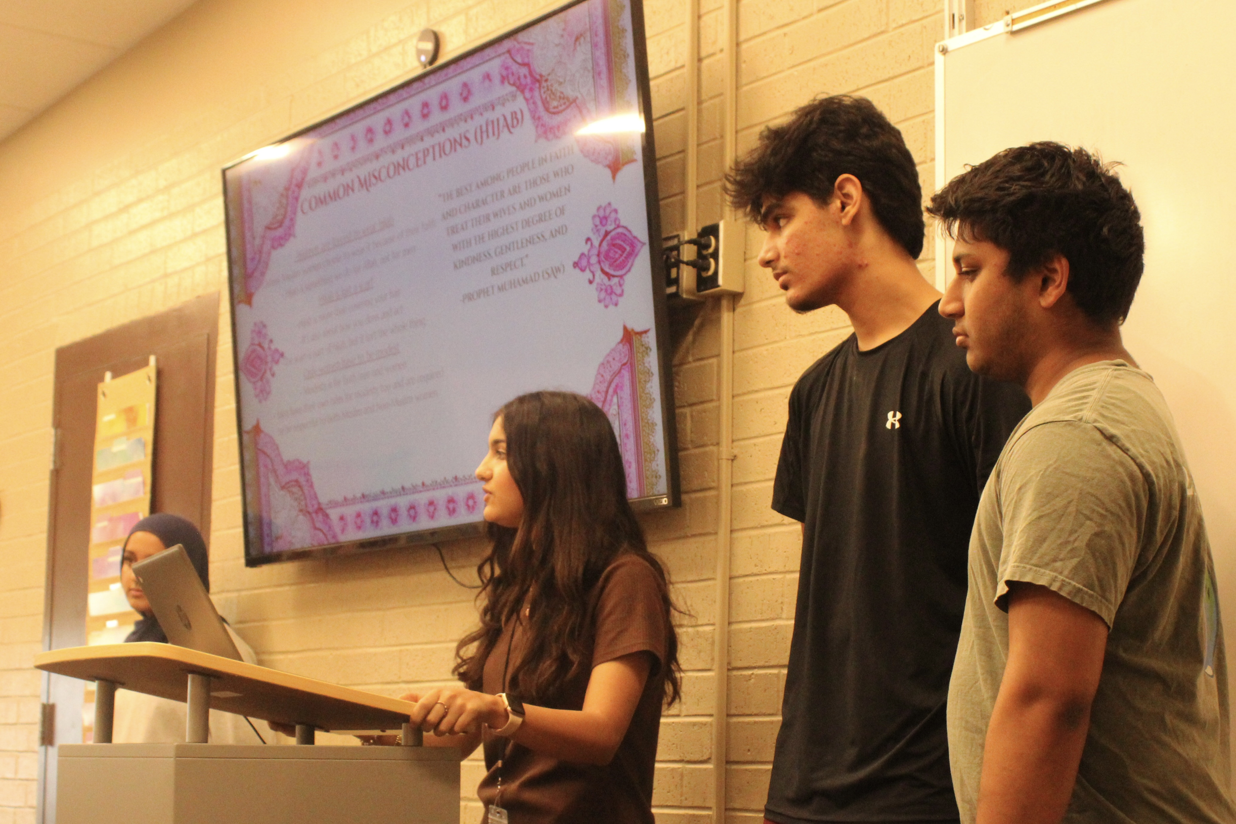 Students stand in front of a TV while presenting slideshow.