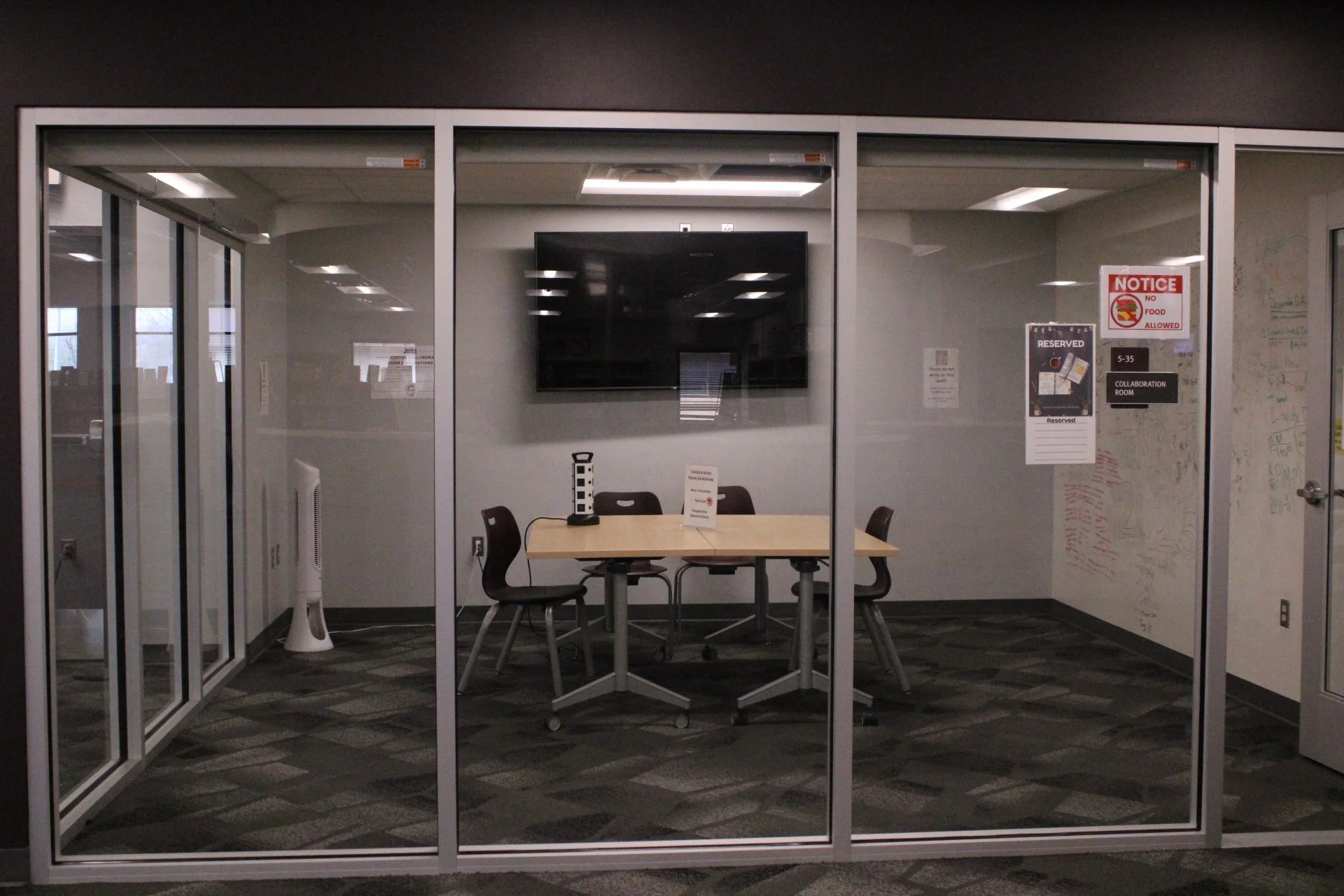 A room with glass walls that has a collaboration table in the middle of the room.