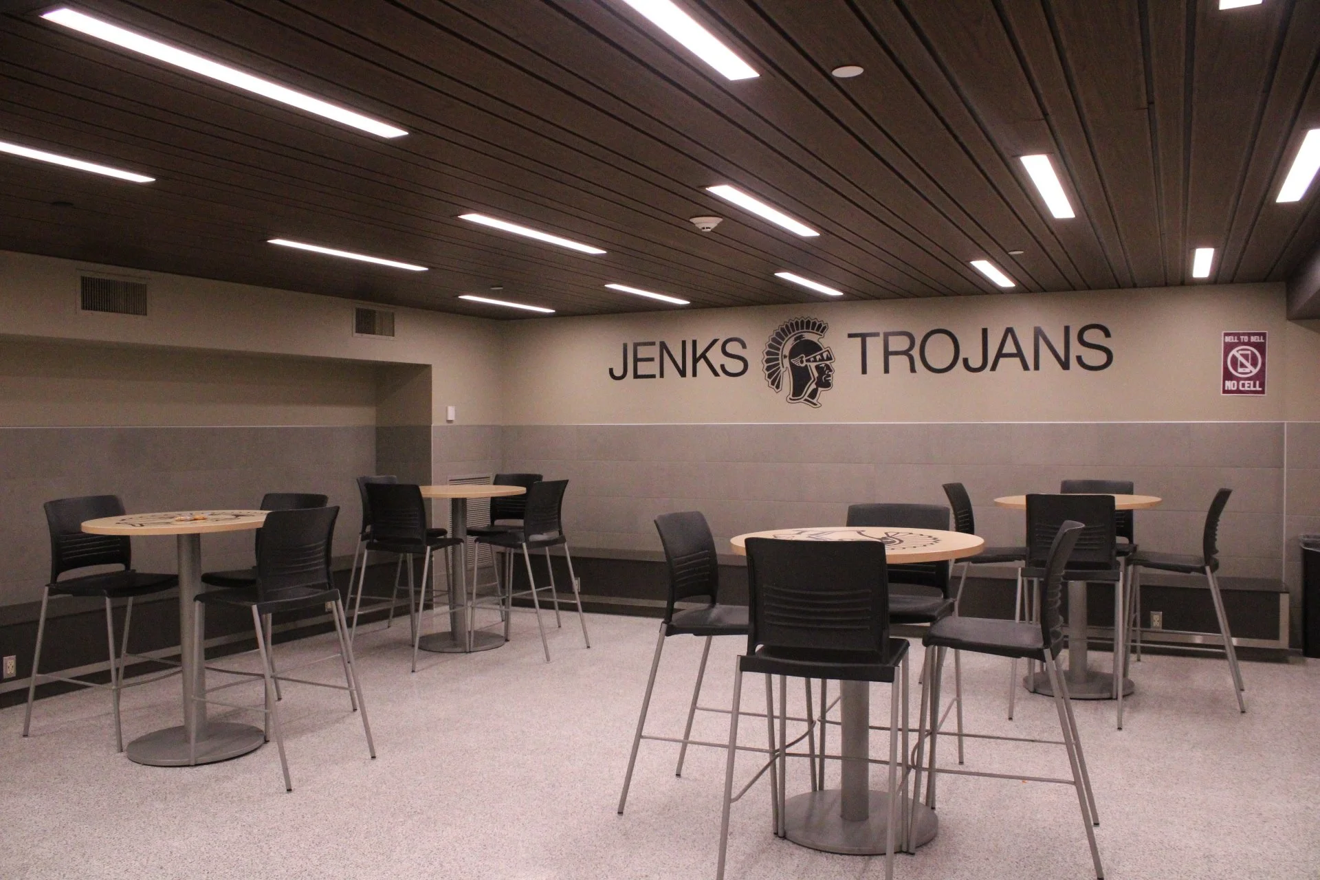 Common space with benches along the walls and small, high-top tables with chairs around them in the middle of the common space.