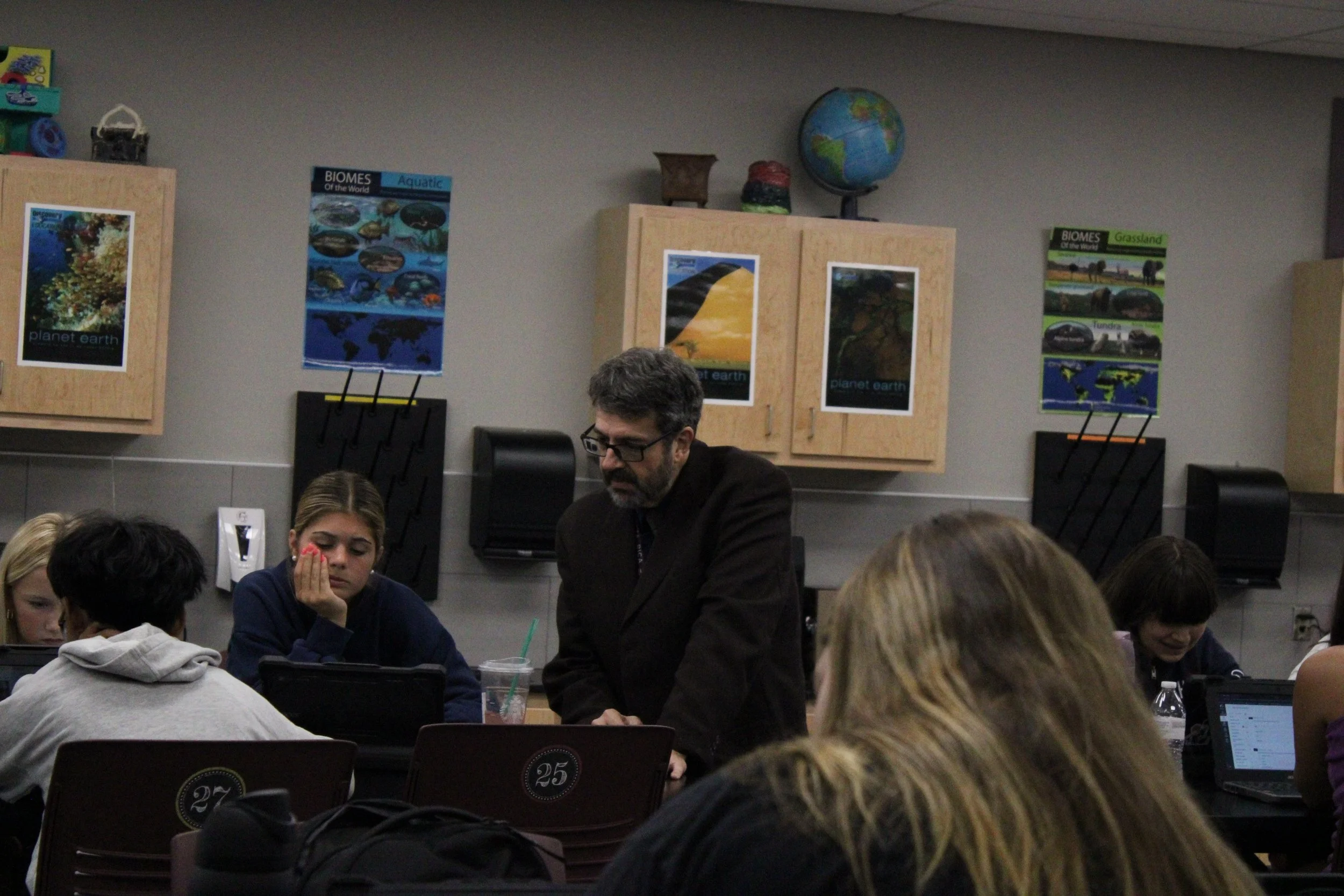 students with chromebooks do a test while a teacher walks between them