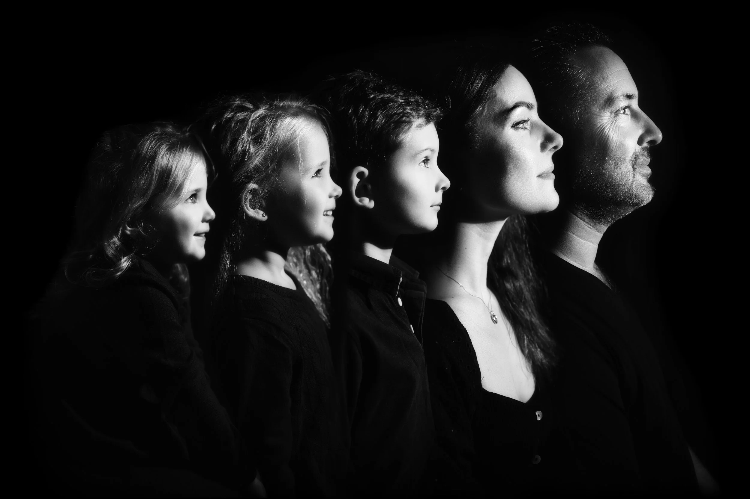 Schwarzweißaufnahme einer Familie, die in einem Seitenprofil abgebildet ist, mit Licht, das jede Person nacheinander beleuchtet.