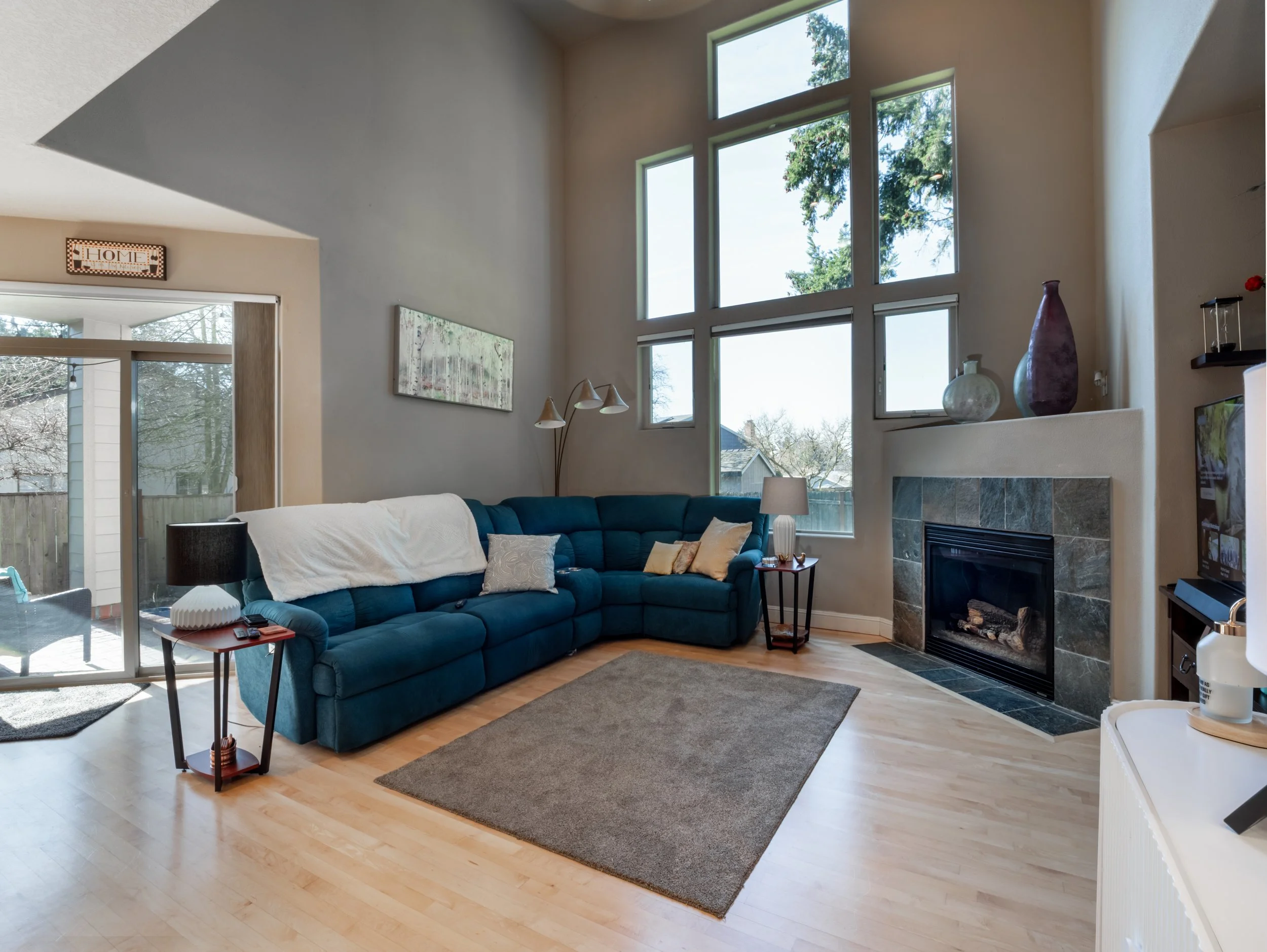 Living room with large blue sectional sofa, fireplace with slate tile, tall multi-pane window, and hardwood floors.