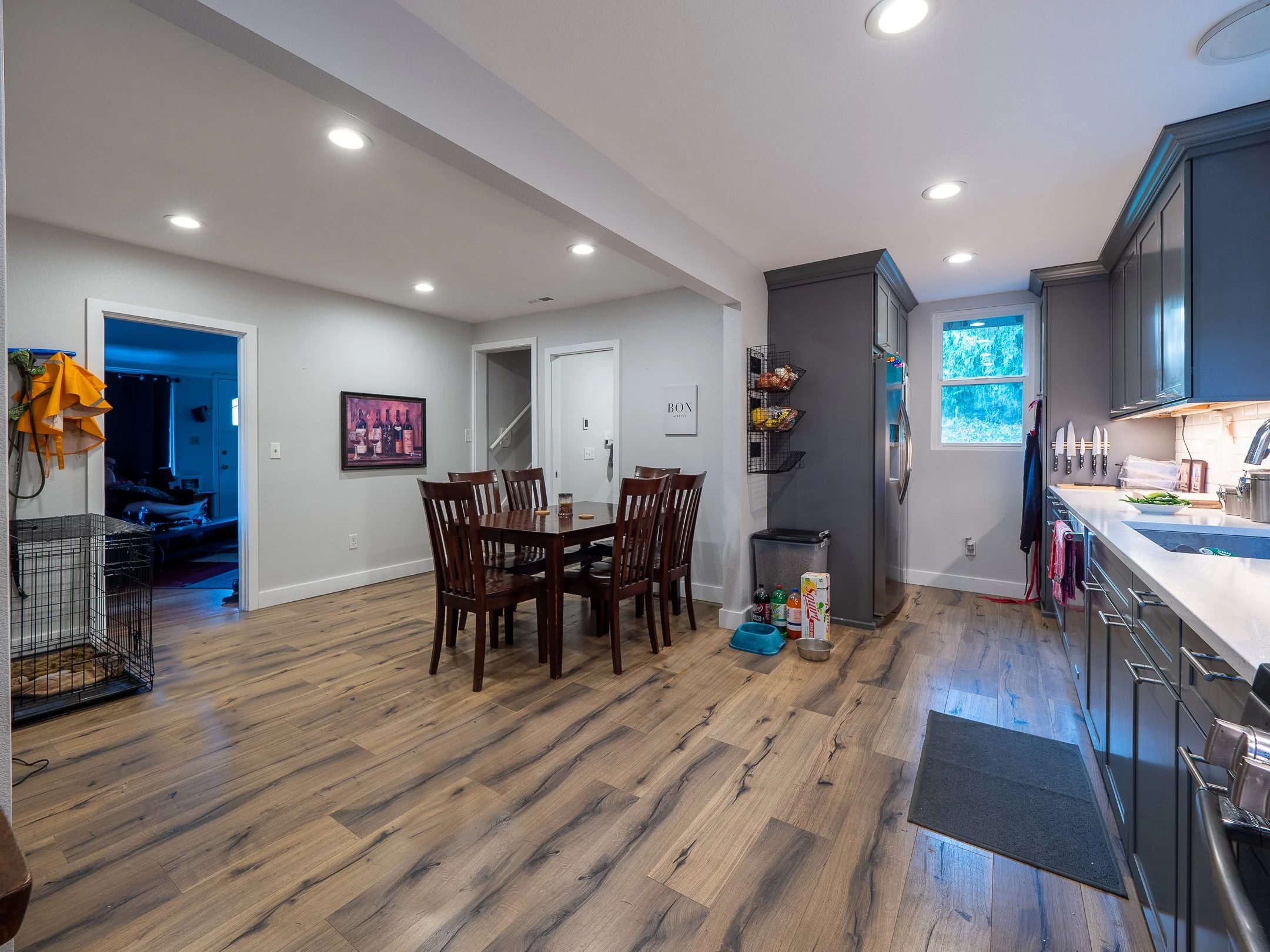Kitchen and dining area with hardwood floors, grey cabinets, refrigerator, window, and a wooden dining table with six chairs.