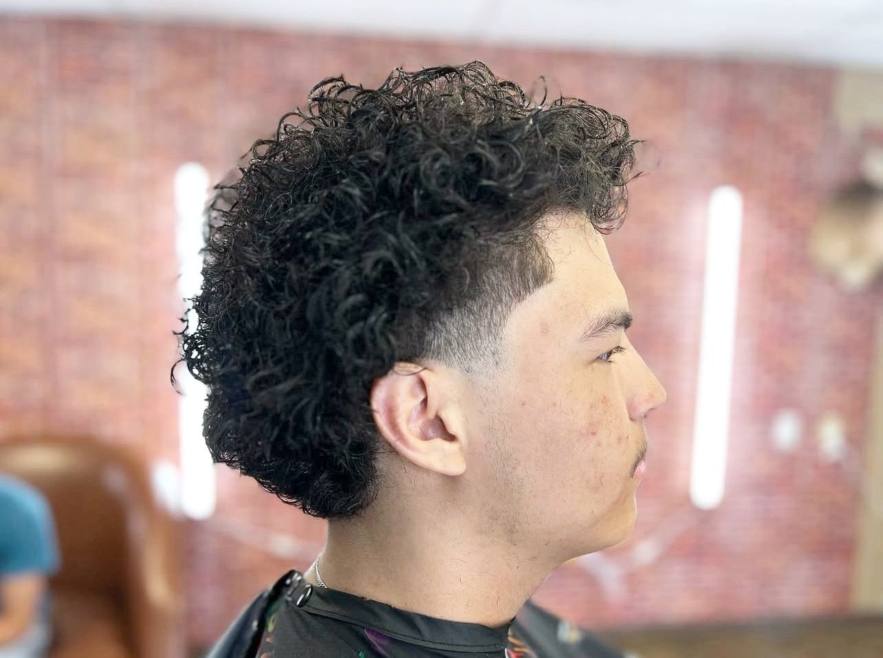 Person with curly undercut hairstyle in a barbershop.