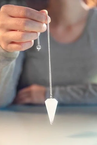Person holding a silver necklace with a white crystal pendant.