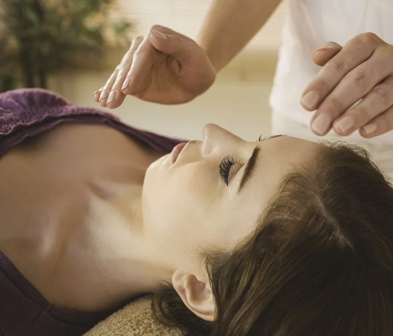 A woman receiving an acupuncture treatment with fine needles on her face and neck, lying down with her eyes closed.