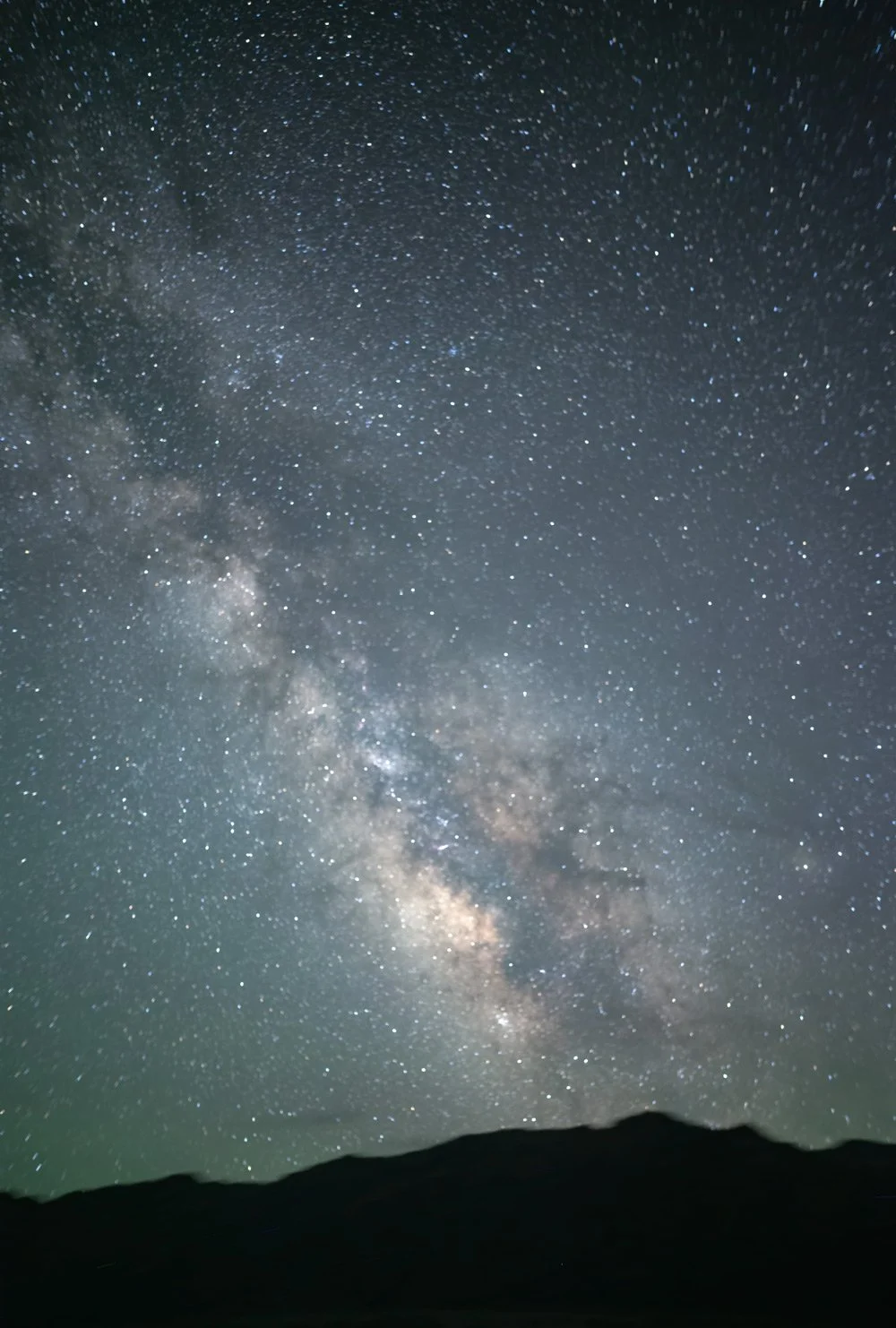A resplendent Milky Way arches over the silhouetted Cottonwood Mountains at Mesquite Flats in Death Valley, California.