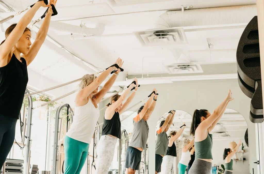 Group of women performing overhead arm exercises on reformer machines during a Pilates class in Squamish studio
