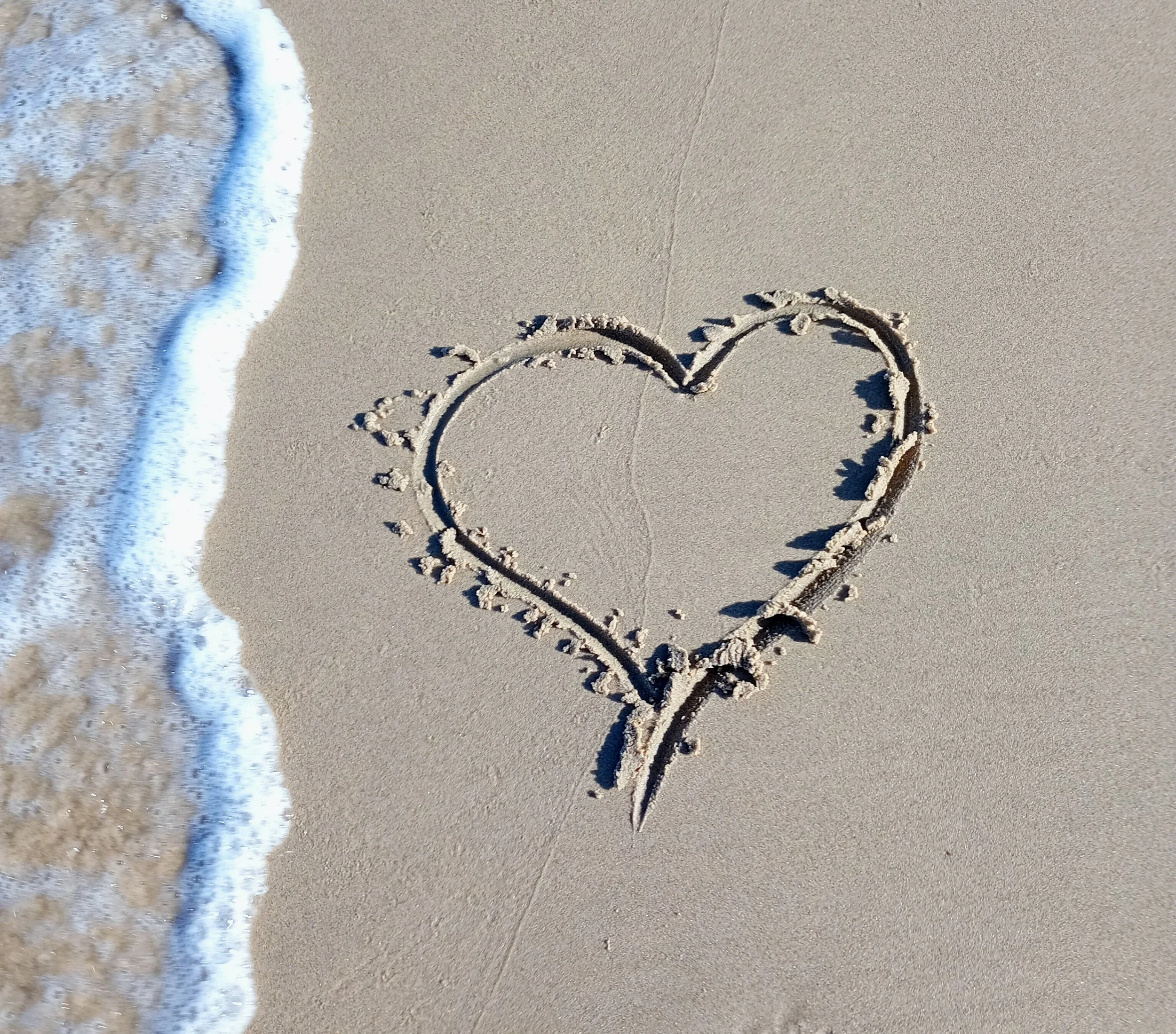Hearts drawn in wet sand with a wave approaching from the left side on the beach.