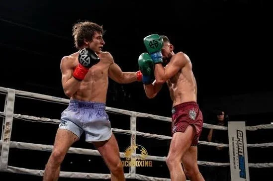 Two male boxers in a ring throw punches at each other, wearing gloves and shorts, during a match.