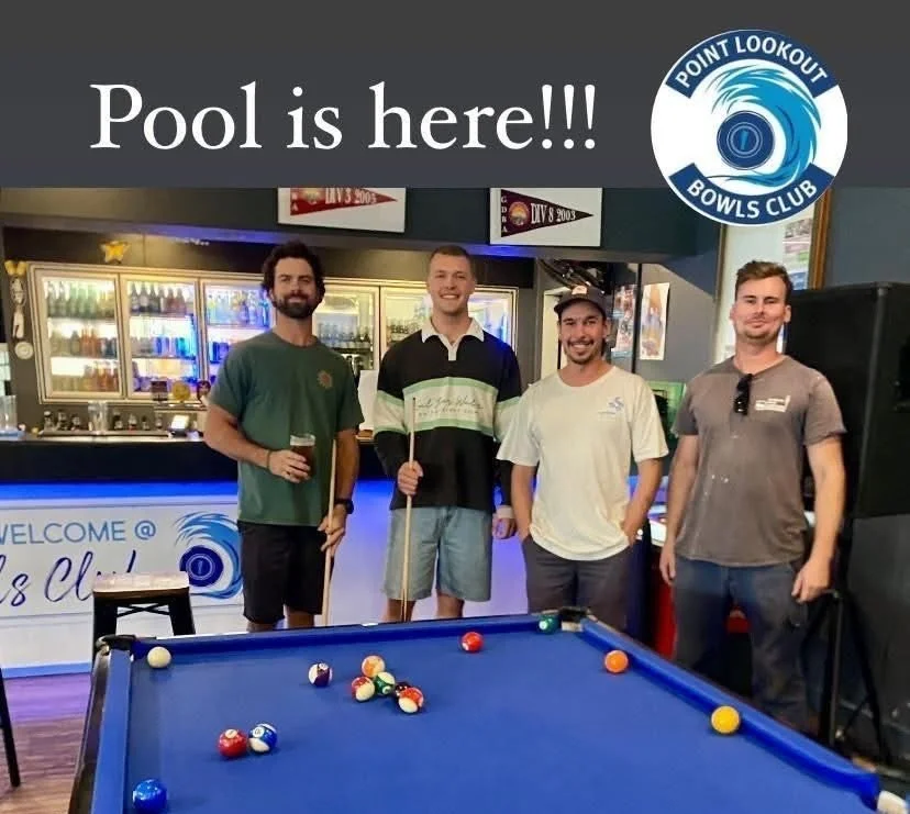 4 men standing round a pool table smiling holding pool cues or a beer
