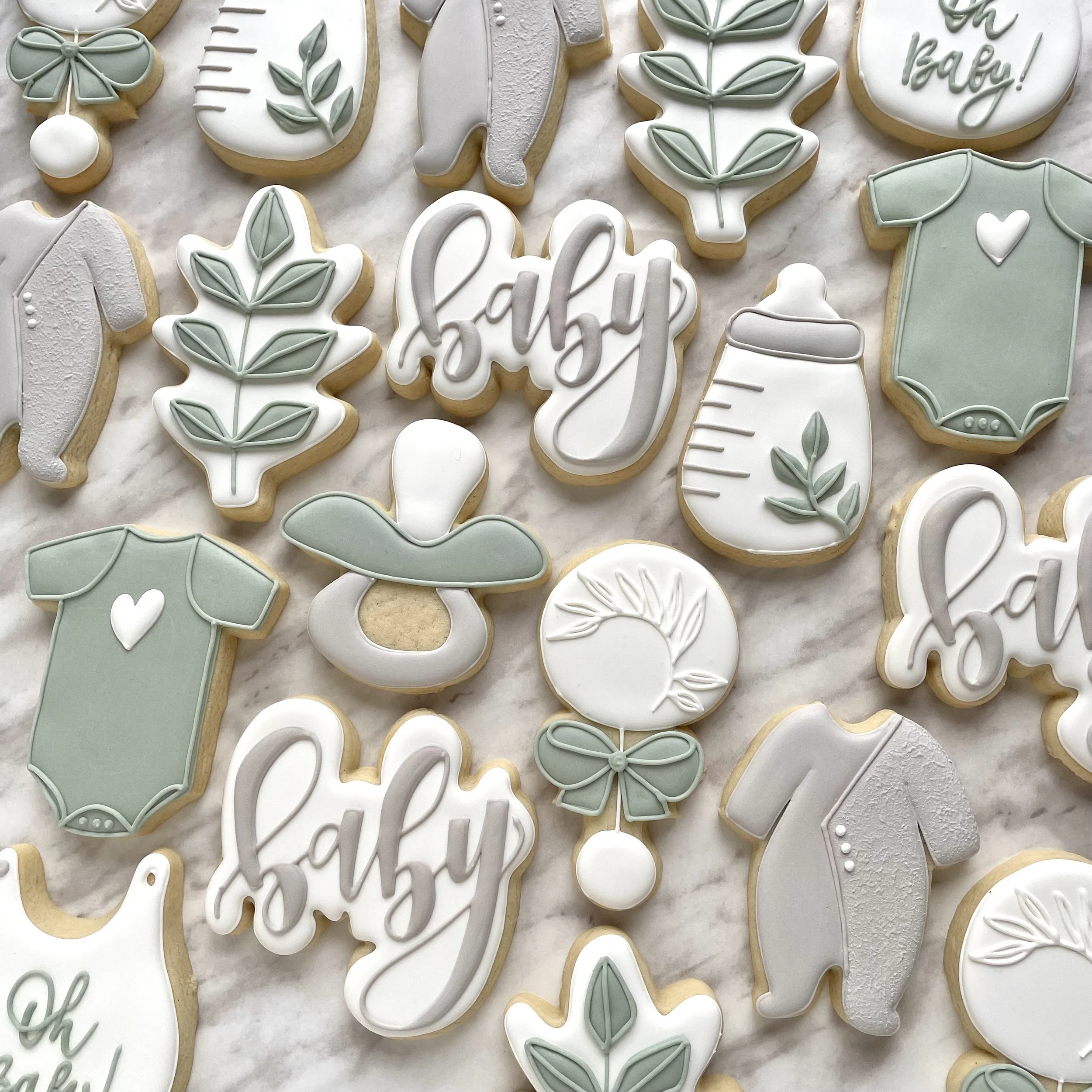 Custom handmade baby shower cookies with cute pastel colors and shaped as onesies, baby bottles, pacifiers, leaves, and the word "baby" in script. Baby shower favours individually wrapped.