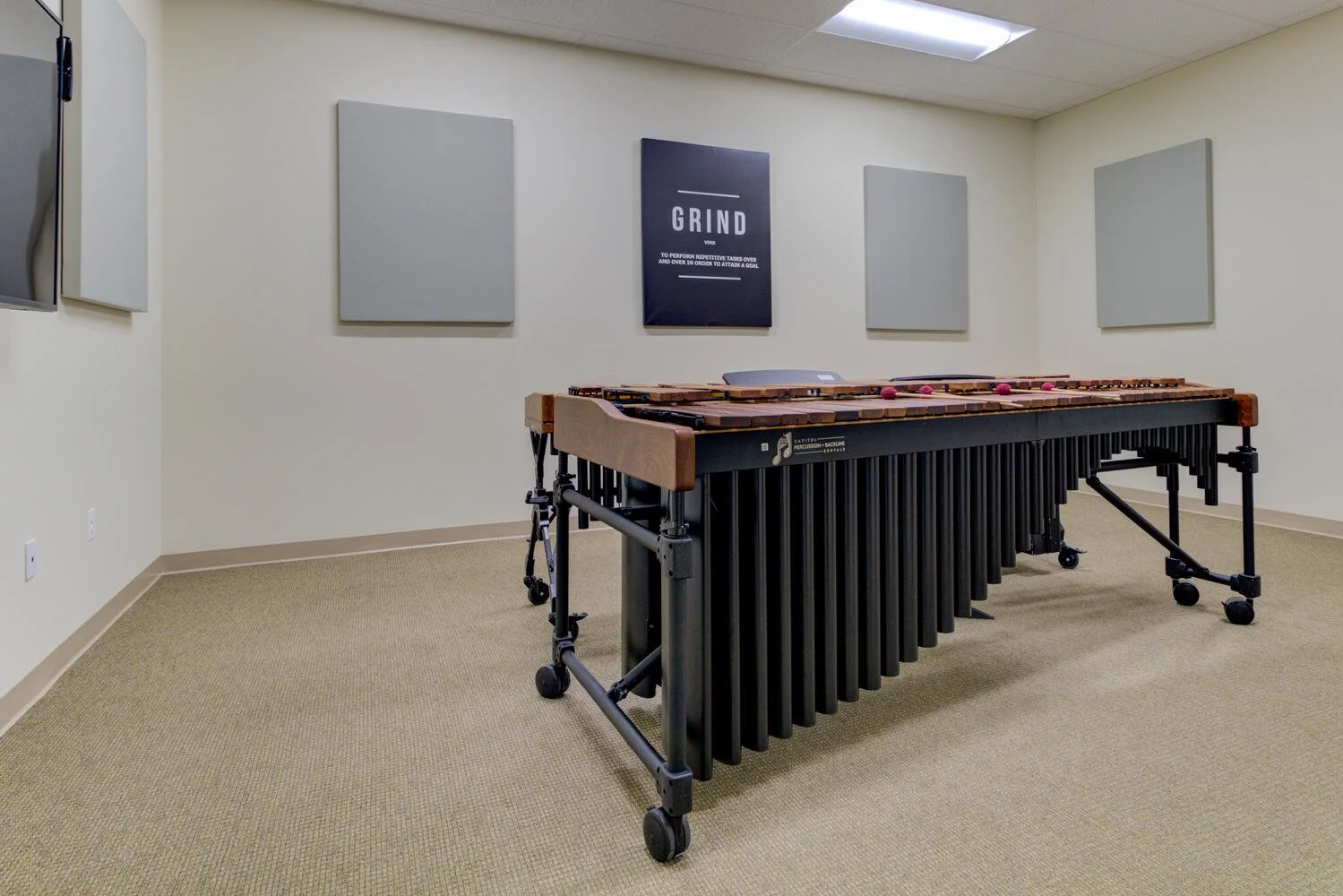 A percussion marimba in a music practice room with four gray soundproof panels on the wall and a motivational poster that says "GRIND".