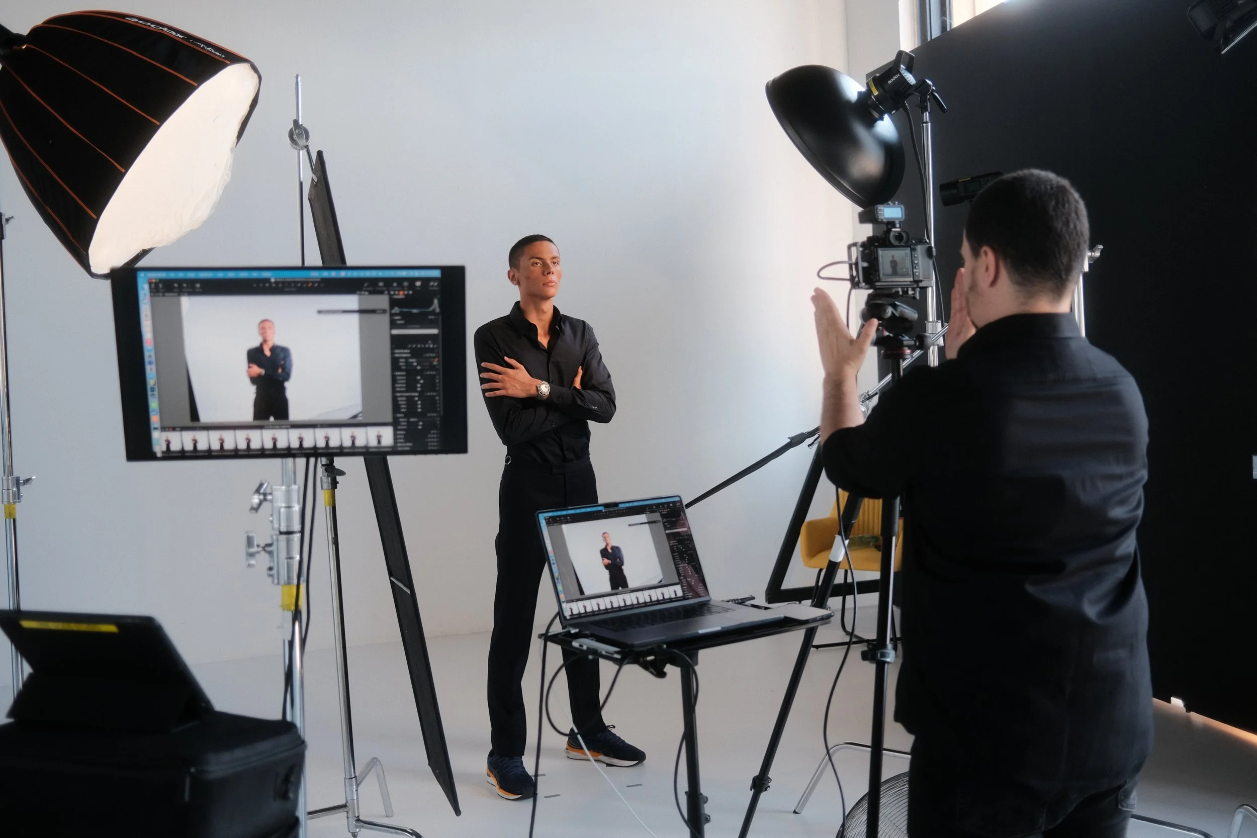 A woman in a black shirt posing during a photo shoot with studio lights and equipment around her.