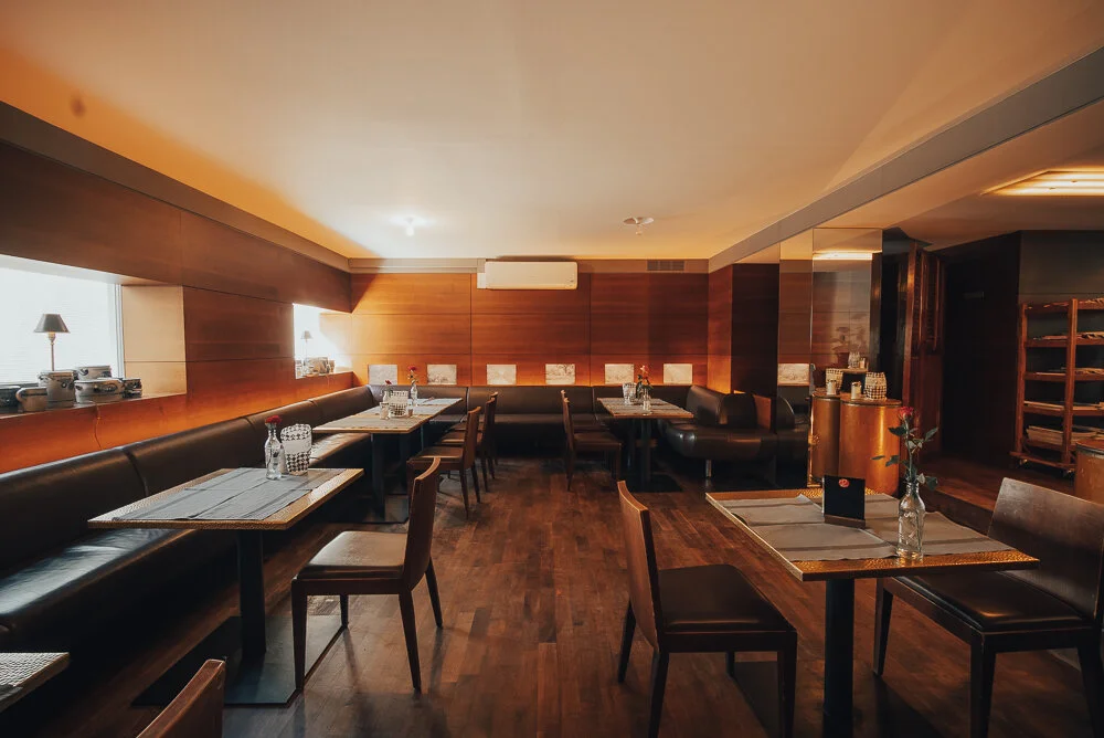 Modernes Restaurant-Interieur mit Holzdesign, Tischen, Stühlen und dekorativen Pflanzen.