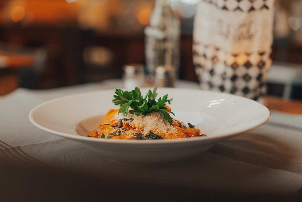 Ein Teller mit Pasta, garniert mit Käse und frischen Kräutern, auf einem Tisch in einem Restaurant.